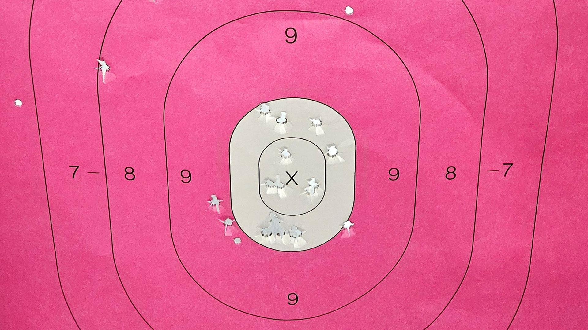 Pink shooting target paper with concentric rings numbered 7 to 9, many bullet holes clustered near the center X.