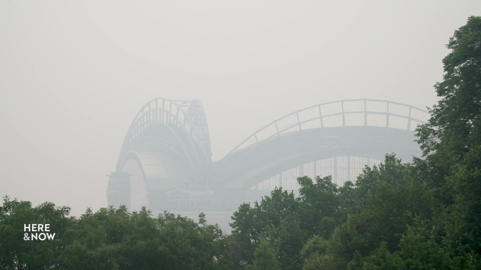 A still image shows a bridge covered in a thick layer of fog behind a line of trees. A still image shows a bridge covered in a thick layer of fog behind a line of trees.