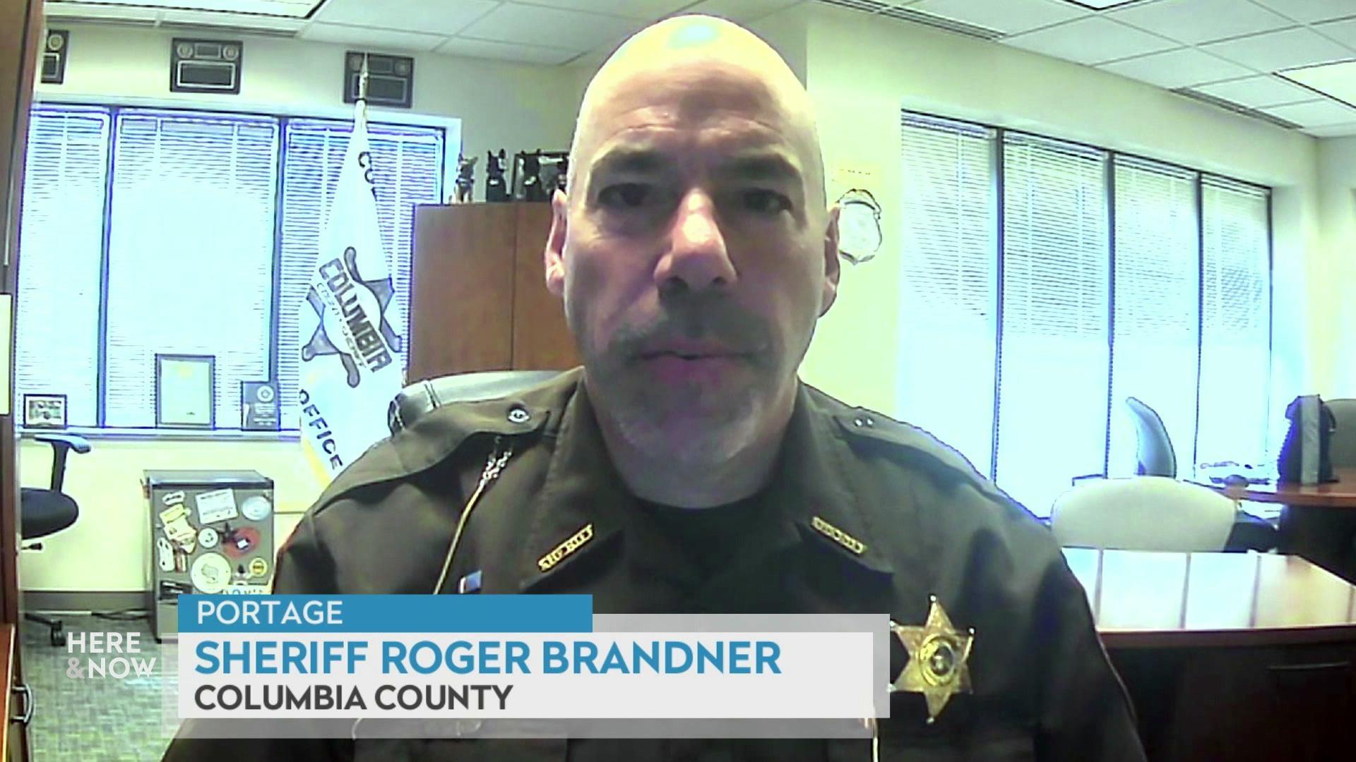 A still image shows Roger Brandner seated in an office with many windows, with a graphic at the bottom that reads 'Portage,' 'Sheriff Roger Brandner' and 'Columbia County.'