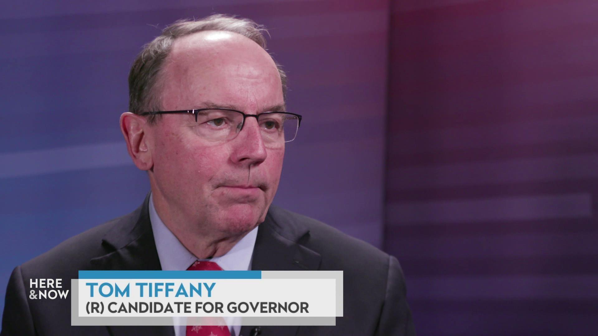 A still image shows U.S. Rep. Tom Tiffany seated on the 'Here & Now' satellite set featuring a gradient background, with a graphic at the bottom that reads 'Tom Tiffany' and '(R) Candidate for Governor.' A still image shows U.S. Rep. Tom Tiffany seated on the 'Here & Now' satellite set featuring a gradient background, with a graphic at the bottom that reads 'Tom Tiffany' and '(R) Candidate for Governor.'