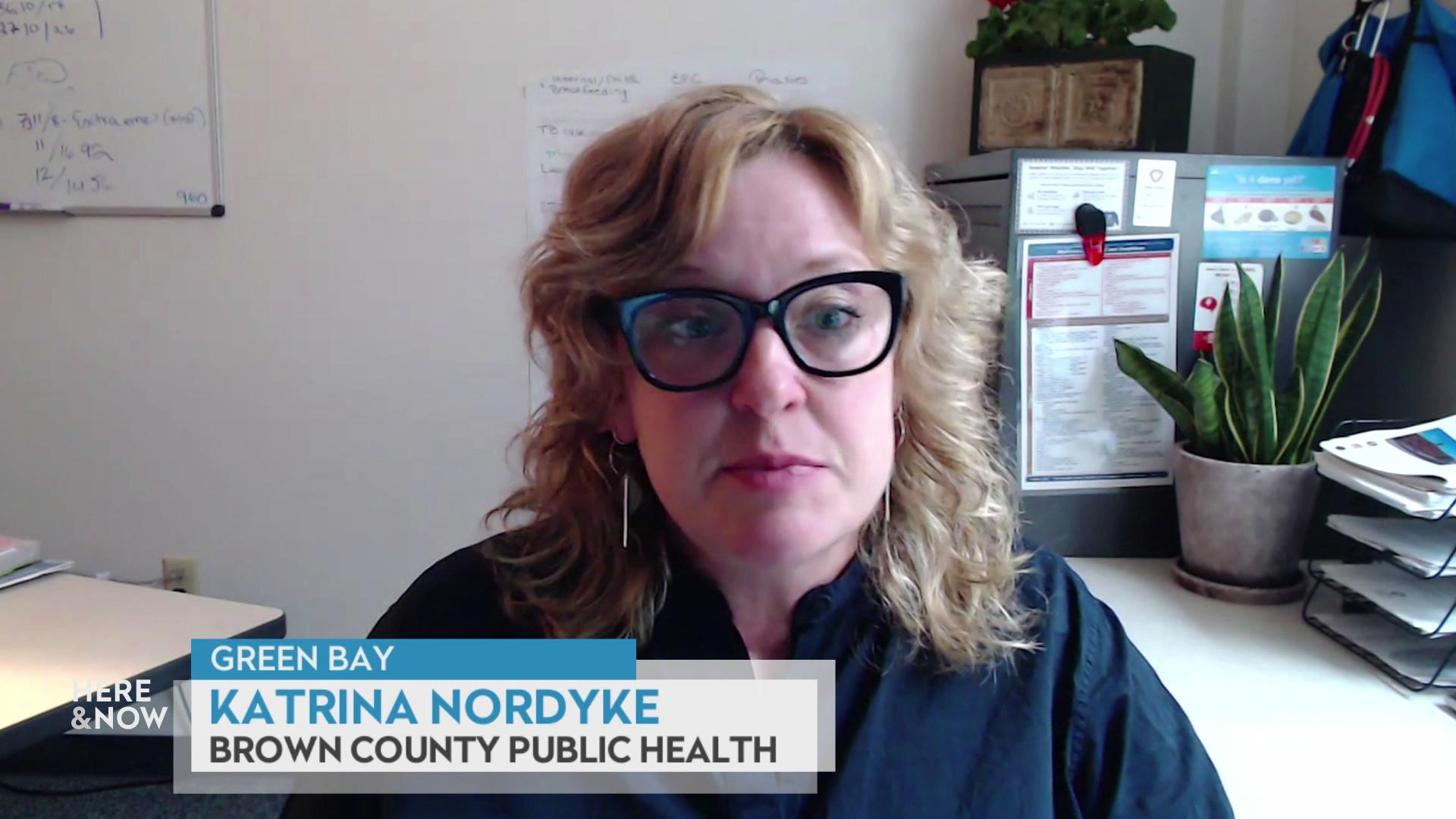 A still image from a video shows Katrina Nordyke standing in front of wall with a potted plant to her right, with a graphic at bottom reading 'Green Bay,' 'Katrina Nordyke,' and 'Brown county Public Health.'