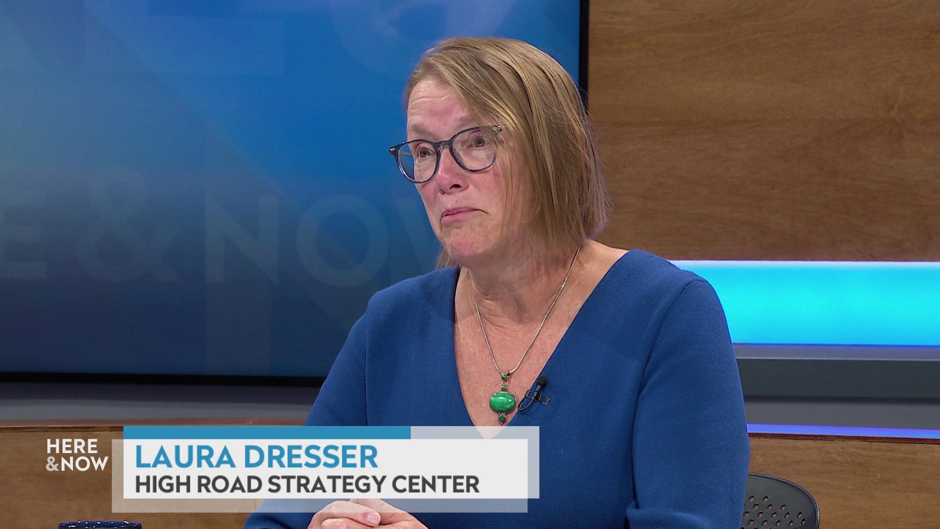 A still image shows Laura Dresser seated at the 'Here & Now' set featuring wood paneling, with a graphic at bottom reading 'Laura Dresser' and 'High Road Strategy Center.'