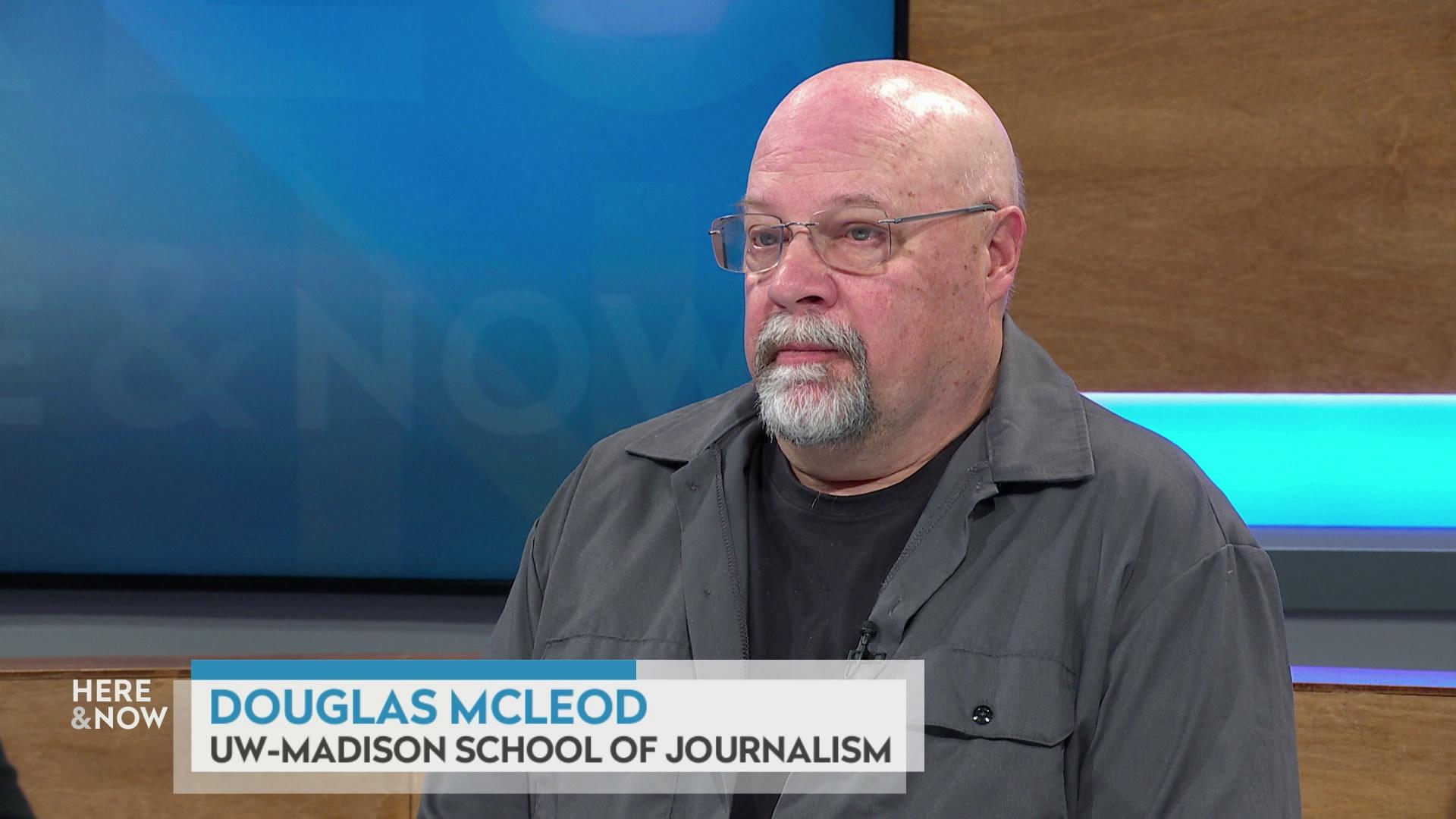 A still image shows Douglas McLeod seated at the 'Here & Now' set featuring wood paneling, with a graphic at bottom reading 'Douglas McLeod' and 'UW-Madison School of Journalism.'
