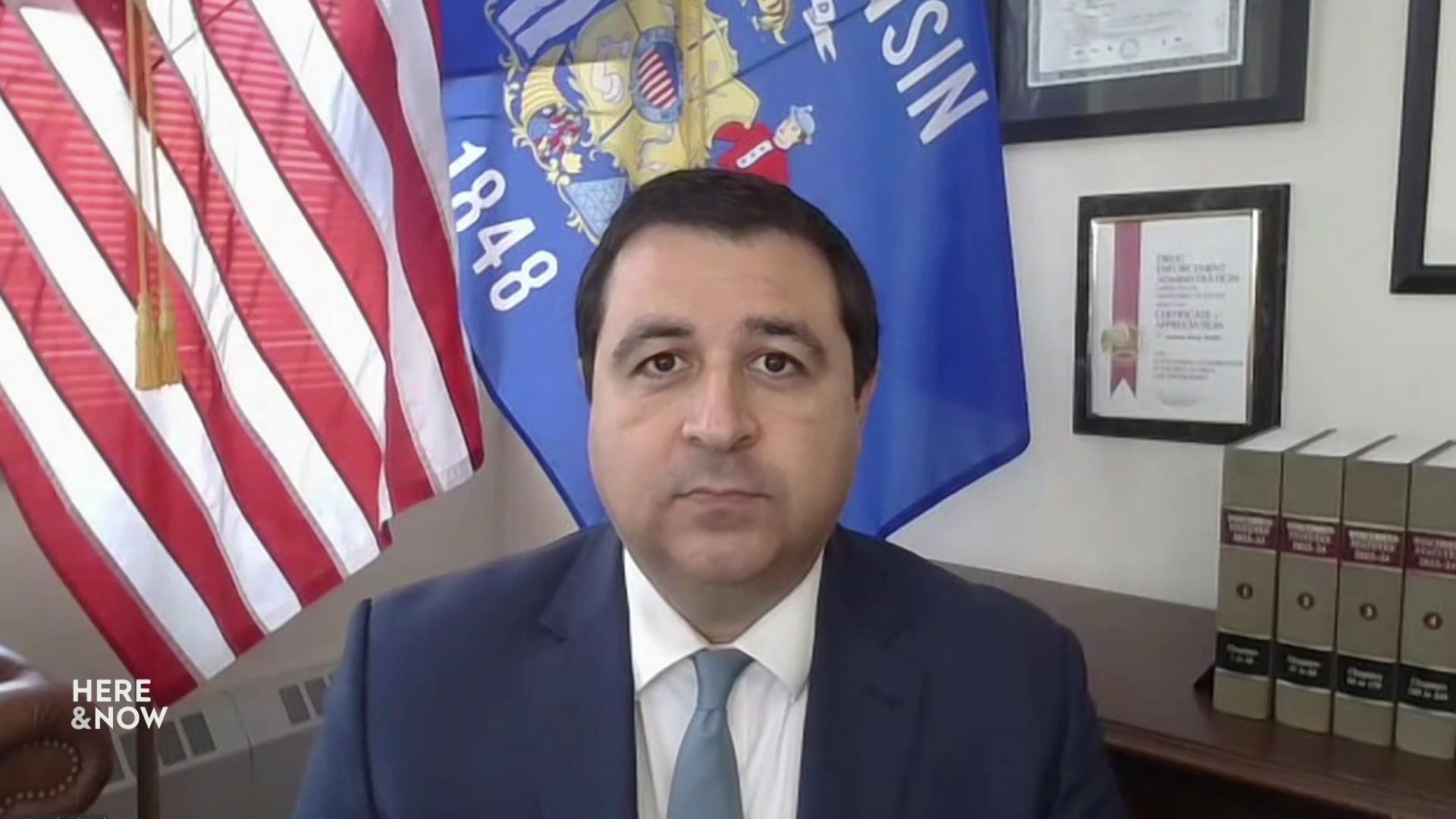 A still image shows Josh Kaul standing in front of the Wisconsin and United States flags.