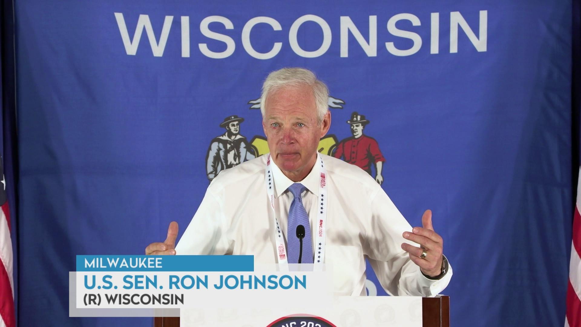 Ron Johnson stands in front of the Wisconsin flag.