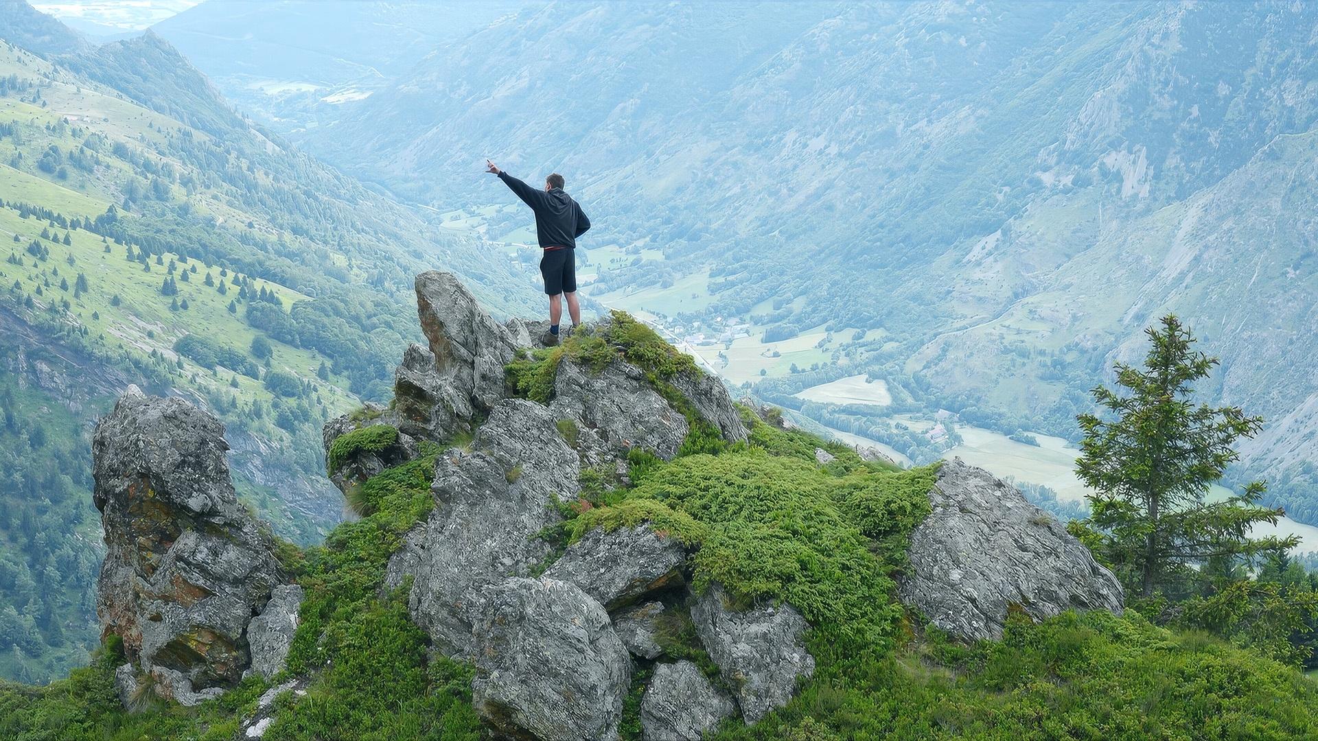 A person standing at the peak of a cliff with one arm raised.