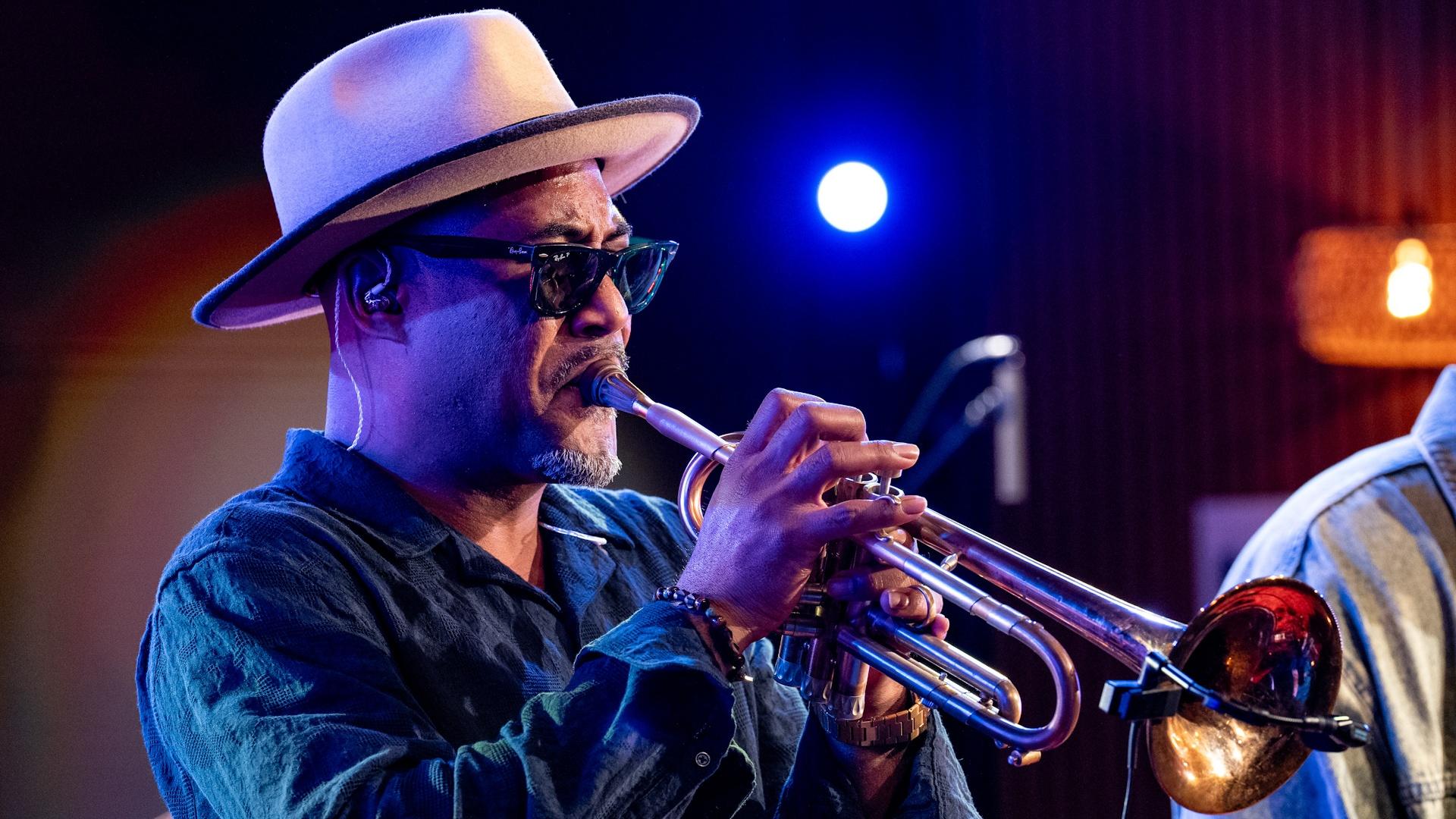 Durham-based jazz musician Al Strong playing a trumpet, wearing a hat and sunglasses.
