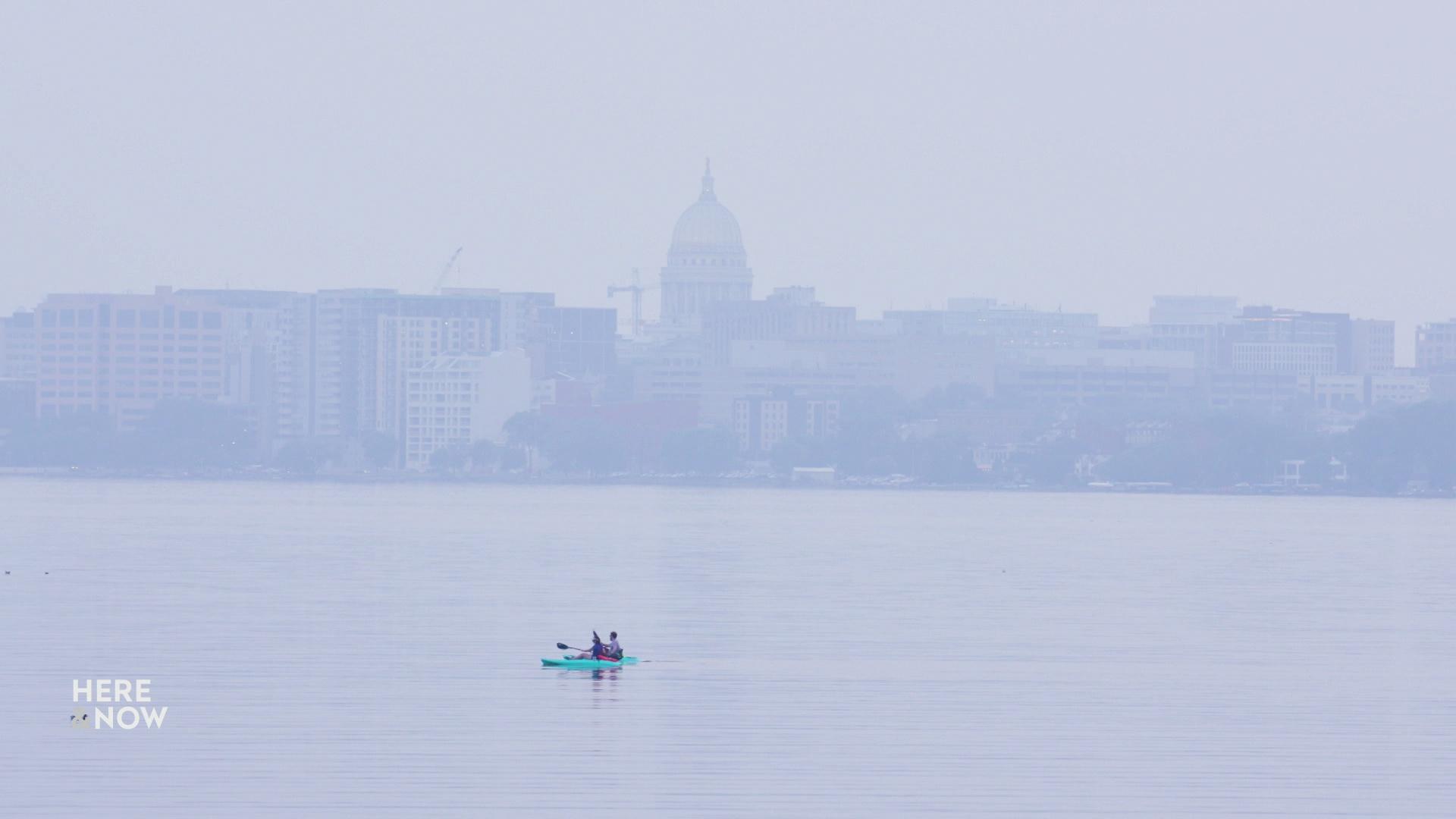 An image shows a hazy skyline of Madison behind water with a single kayak in the foreground.