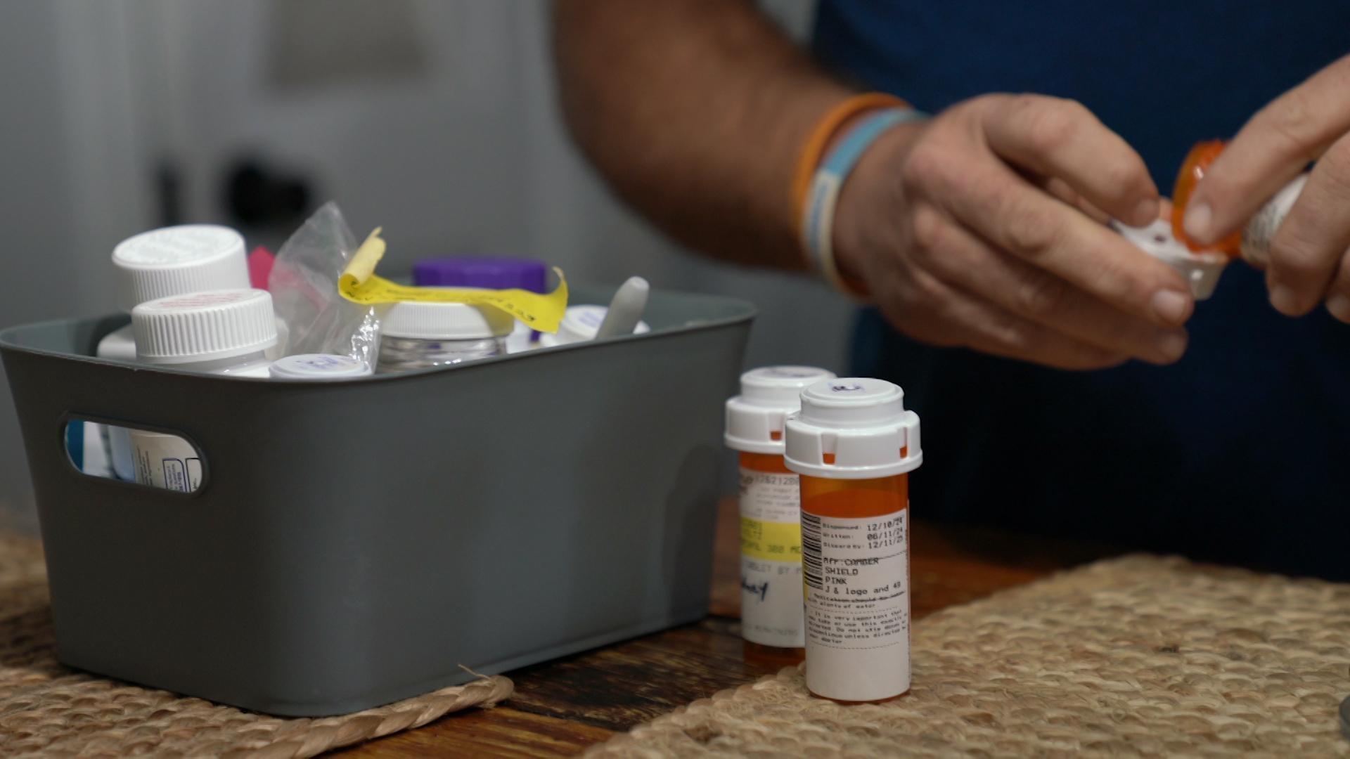 A still image shows Kevin Voltz sorting through his medications from a small gray plastic box.