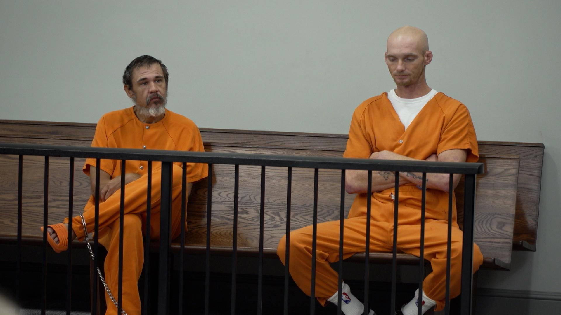 People sitting on a court bench in orange jumpsuits. 