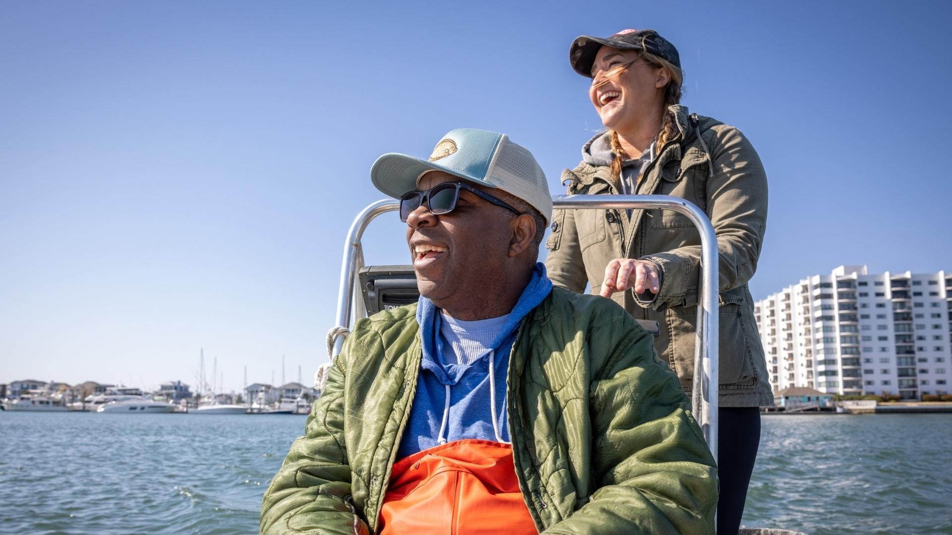 Ana Shellem driving a small motored boat with Ricky Moore at the helm, sitting down.