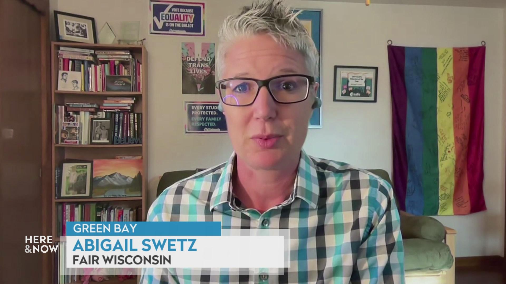 A still image from a video shows Abigail Swetz seated in front of wooden cabinets with books and artwork and a rainbow flag on the wall with a graphic at bottom reading 'Green Bay,' 'Abigail Swetz' and 'Fair Wisconsin.'