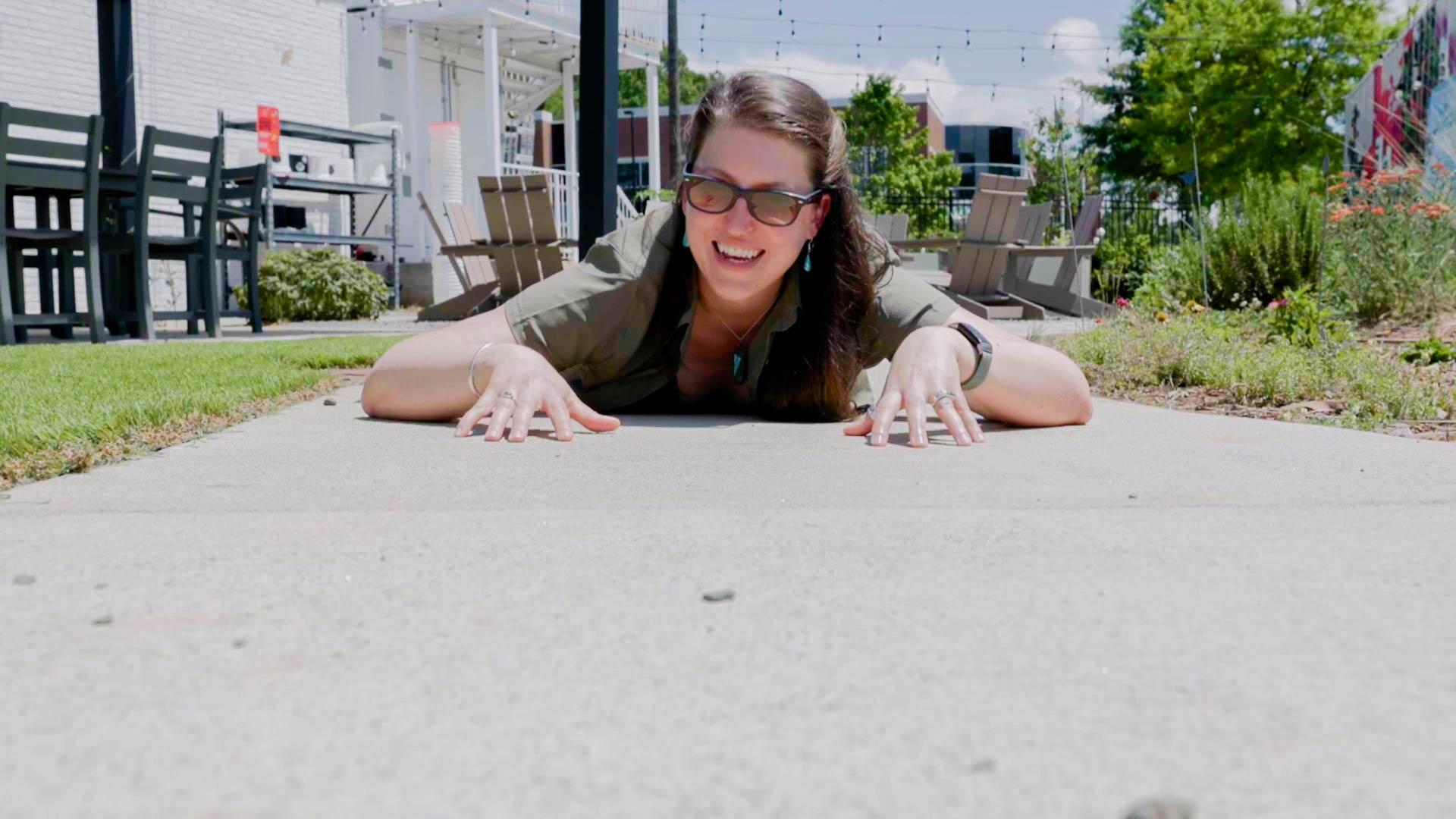 Producer of Sci NC, Michelle Lotker laying on a concrete sidewalk.
