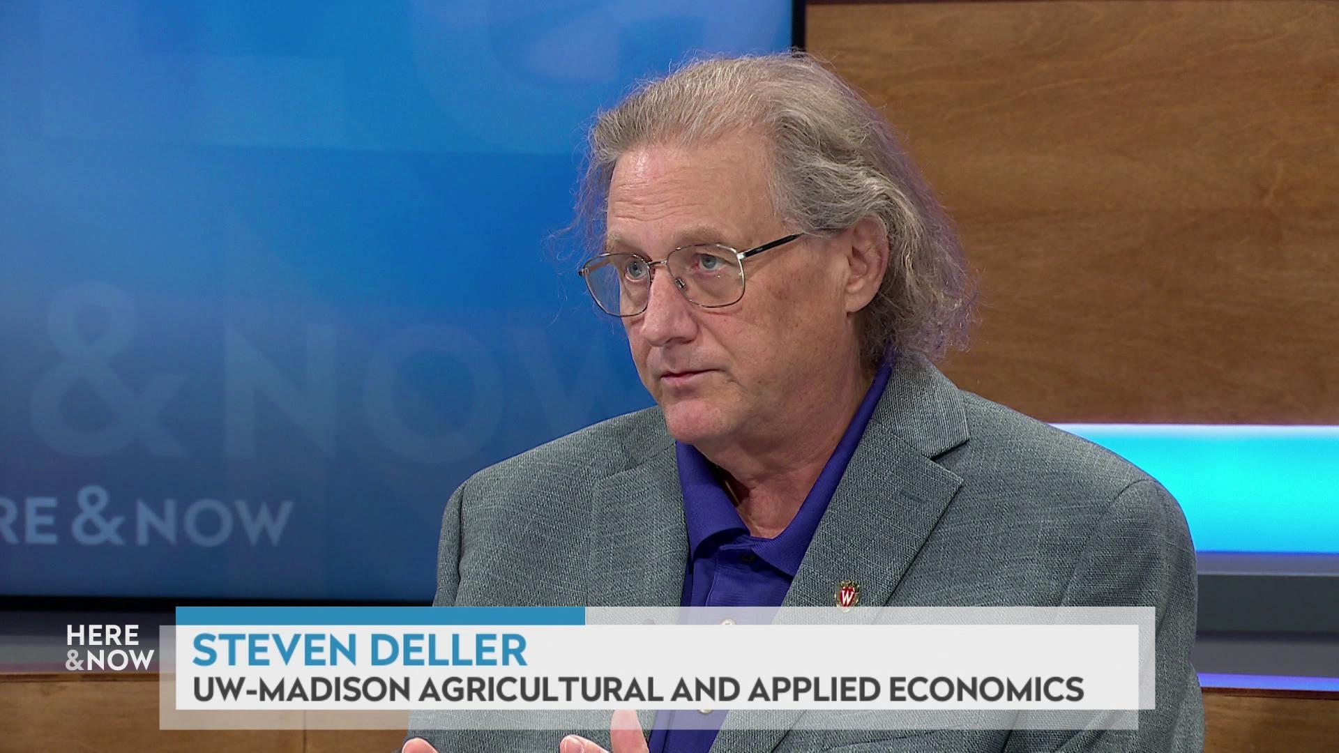 A still image shows Steven deller seated at the 'Here & Now' set featuring wood paneling, with a graphic at bottom reading 'Steven Deller' and 'UW-Madison Agricultural and Applied Economics.'