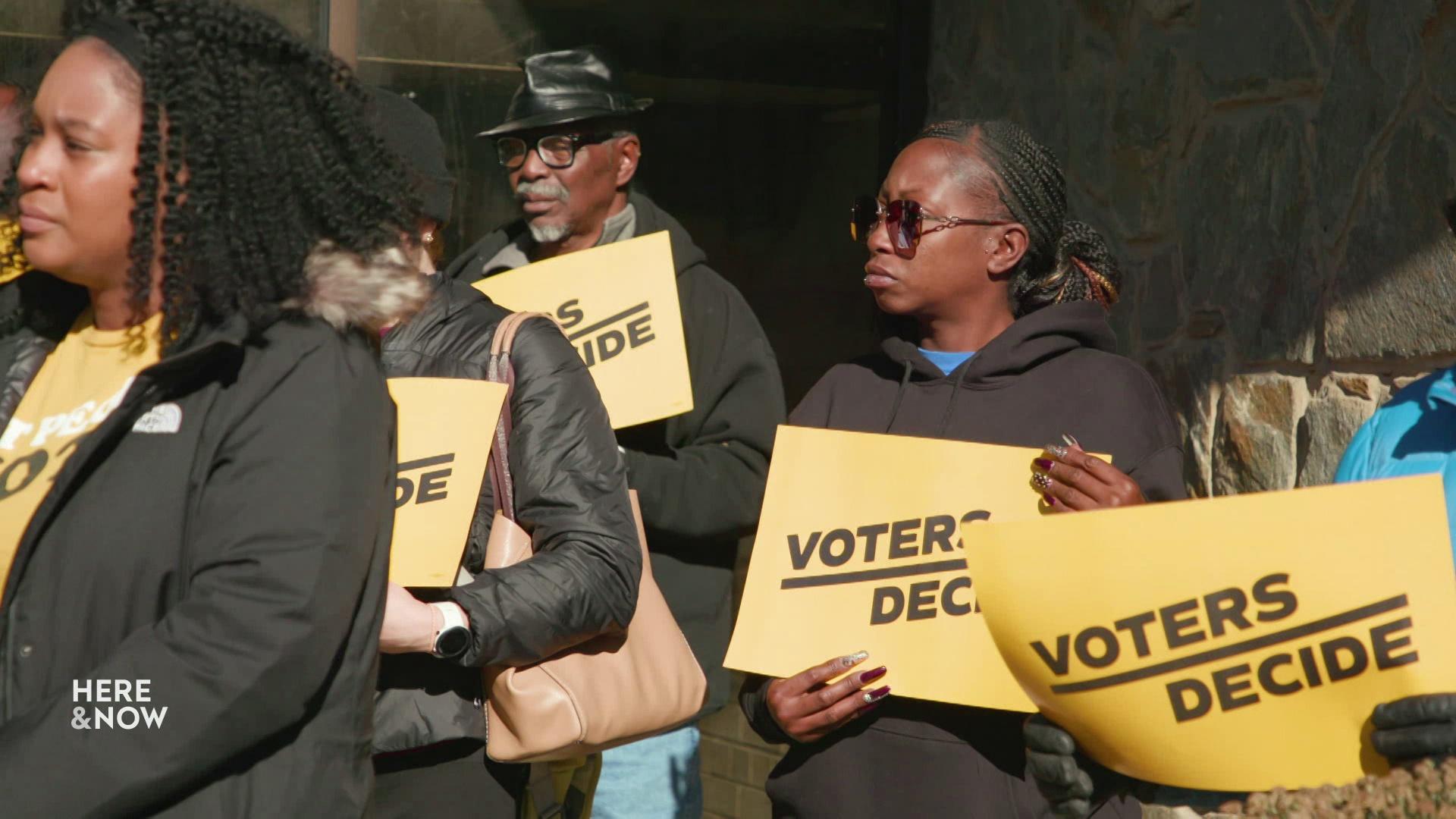 People hold yellow signs reading 'Voters Decide.'