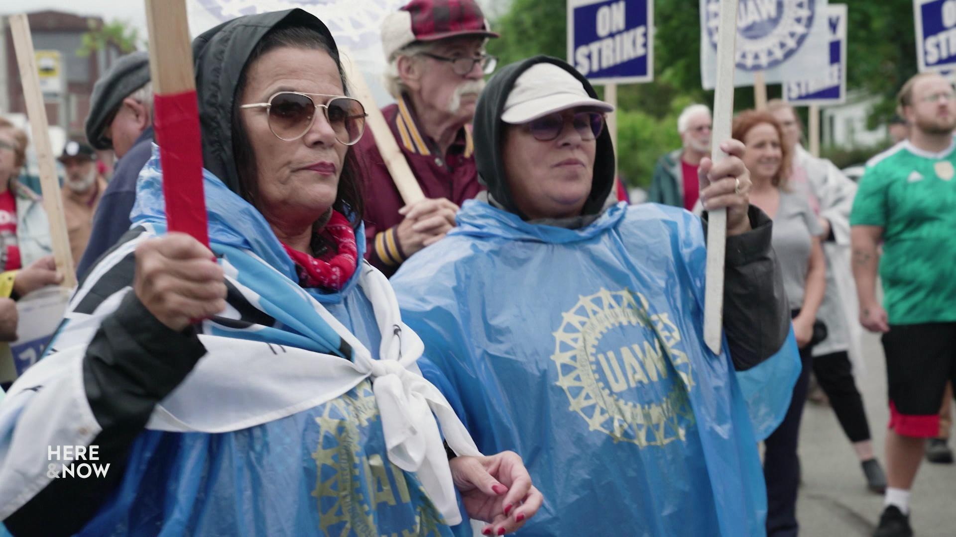 Protesters wear blue ponchos and hold pickets reading 'On Strike.'