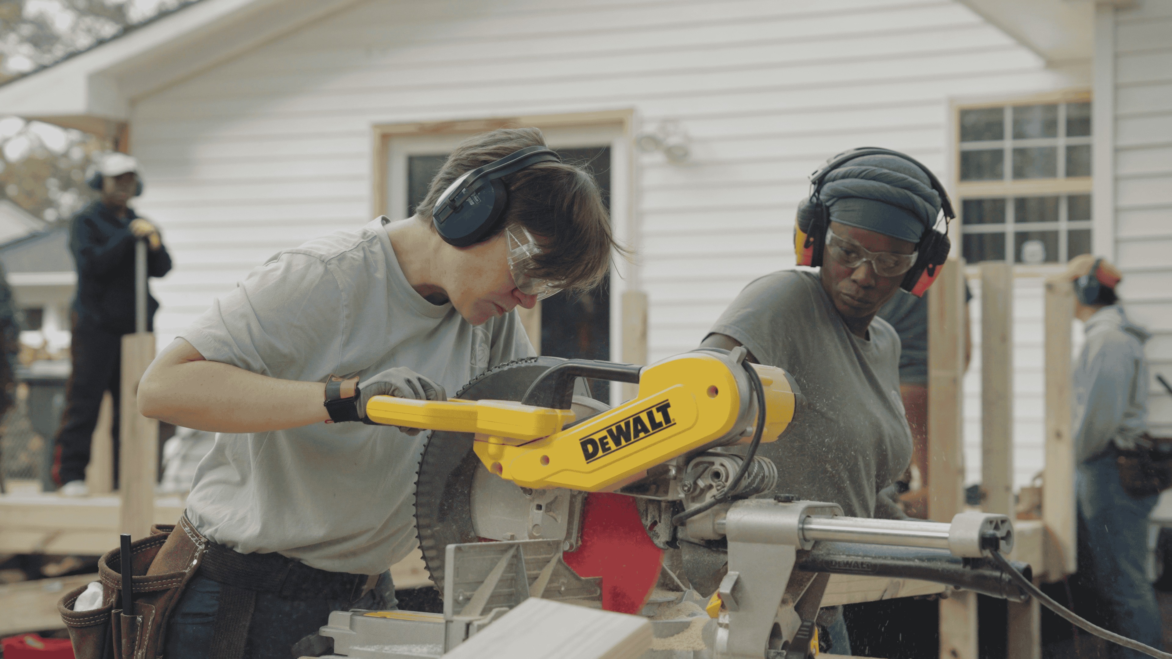 Two people working at a table saw with protective glasses and earphones on.