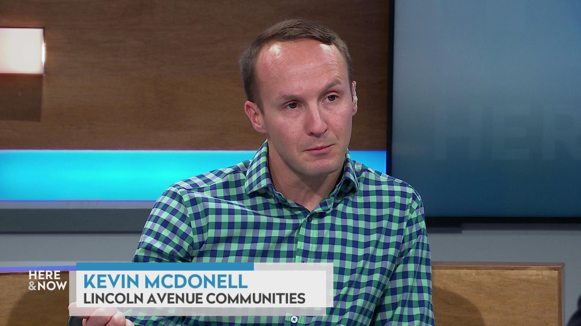 A still image shows Kevin McDonell seated at the 'Here & Now' set featuring wood paneling, with a graphic at bottom reading 'Kevin McDonell' and 'Lincoln Avenue Communities'