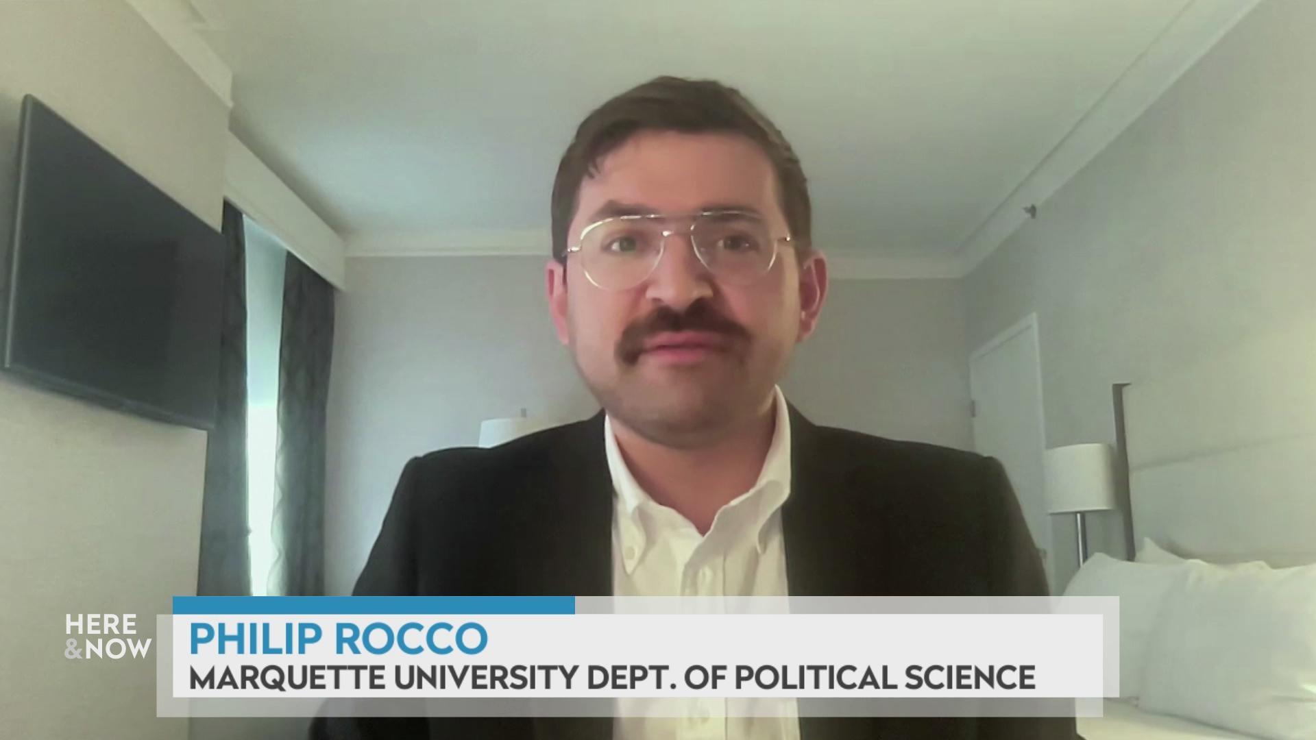 A still image shows Philip Rocco seated in front of a very white bedroom, with a graphic at the bottom that reads 'Philip Rocco' and 'Marquette University Dept. of Political Science.'