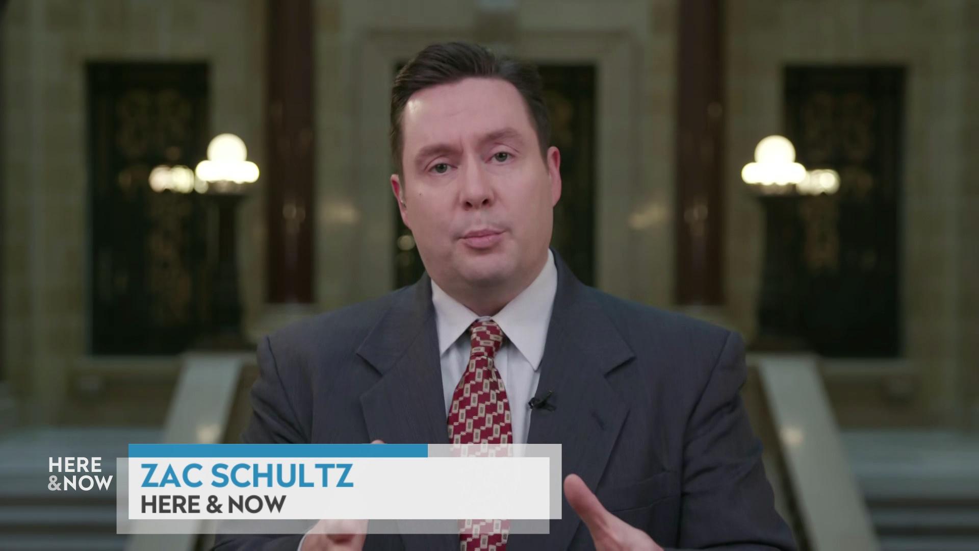 A still image shows Zac Schultz standing in front of the State Capitol rotunda with a graphic at bottom reading 'Zac Schultz' and 'Here & Now.'