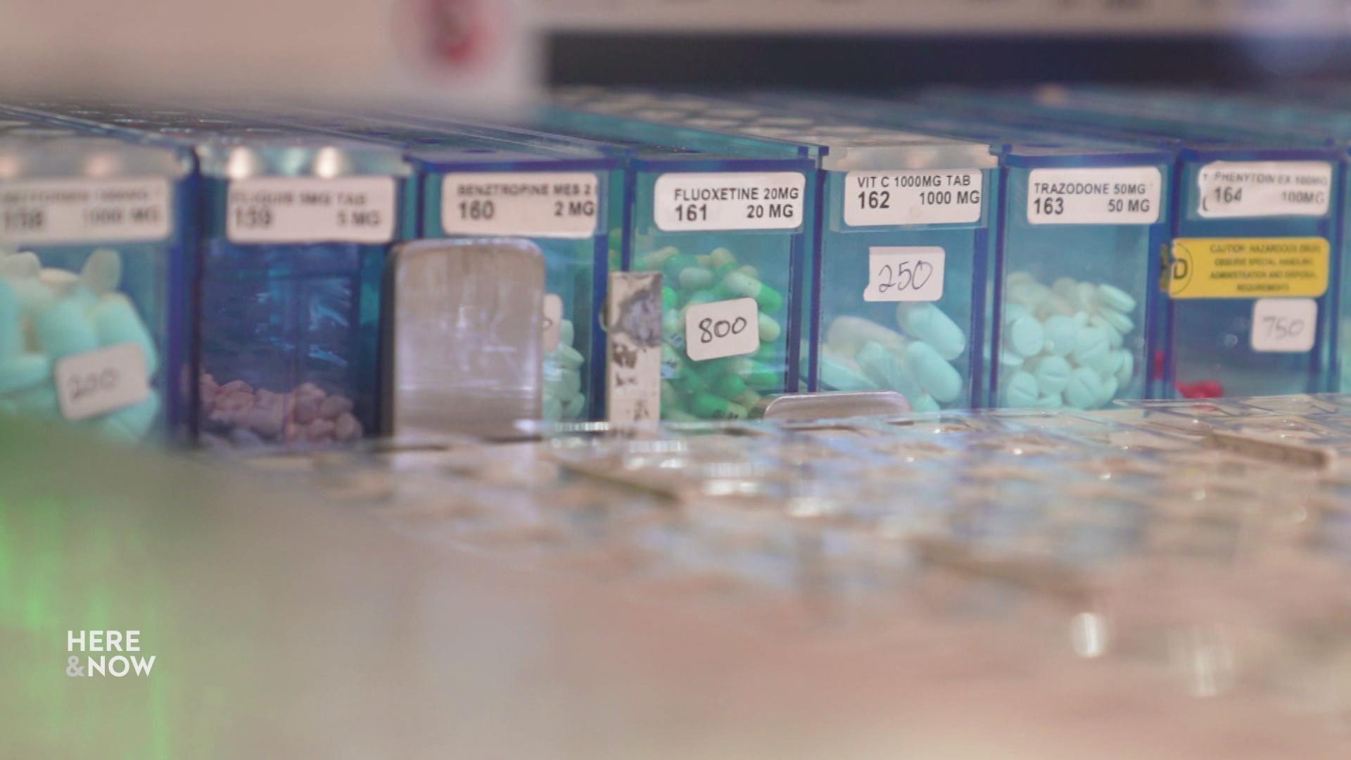 A still image shows rows of semi-opaque blue pill boxes, filled with various pharmaceuticals of different shapes and colors