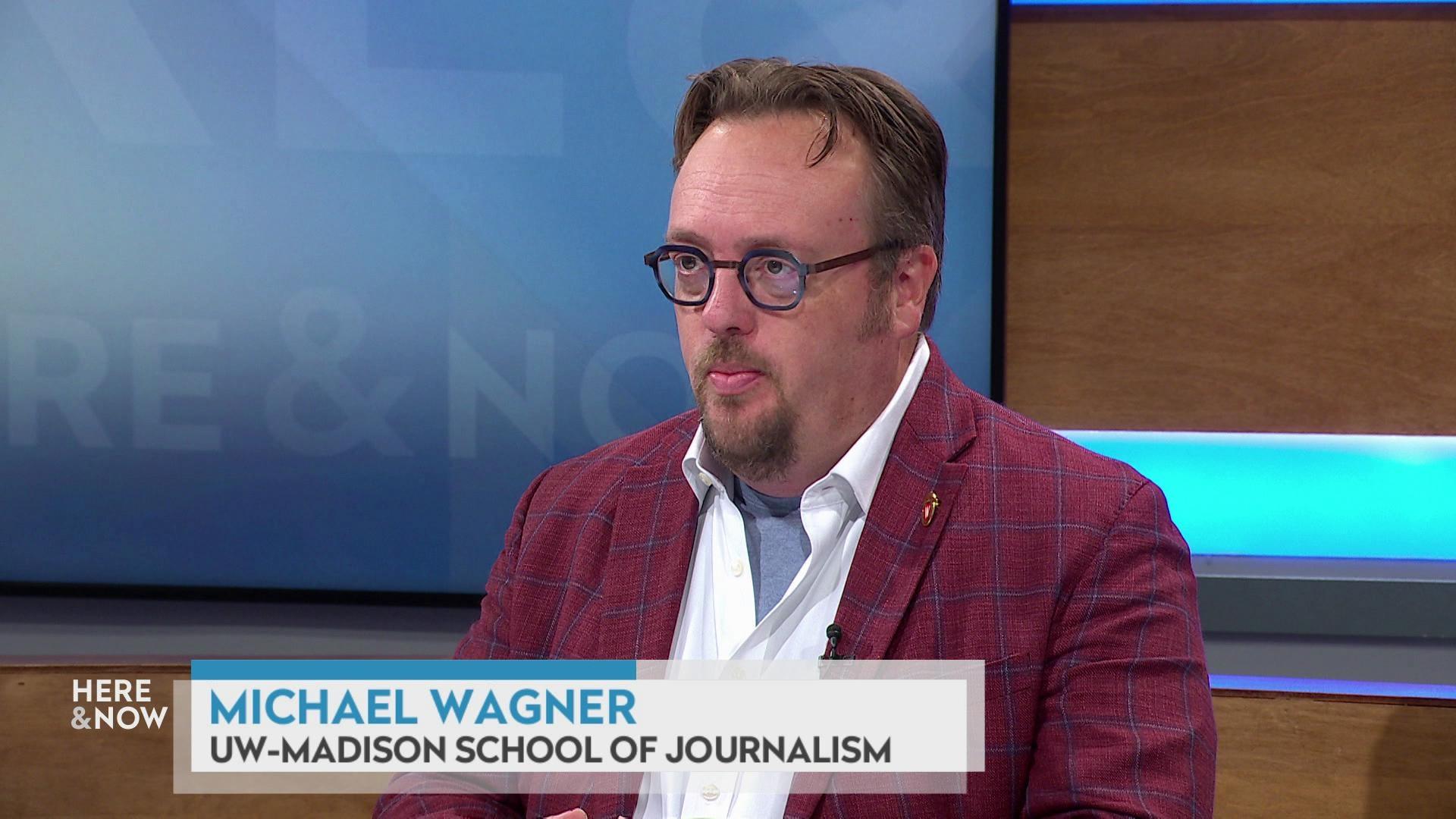 A still image shows Michael Wagner seated at the 'Here & Now' set featuring wood paneling, with a graphic at the bottom that reads 'Michael Wagner' and 'UW-School of Journalism.' A still image shows Michael Wagner seated at the 'Here & Now' set featuring wood paneling, with a graphic at the bottom that reads 'Michael Wagner' and 'UW-School of Journalism.'