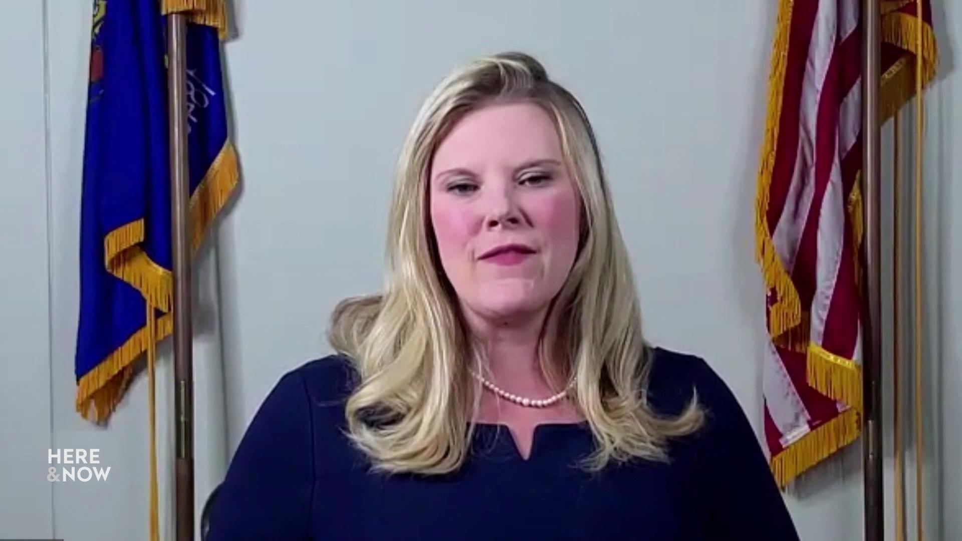 A still image from a video shows Meagan Wolfe seated between the Wisconsin state flag and U.S. flag.