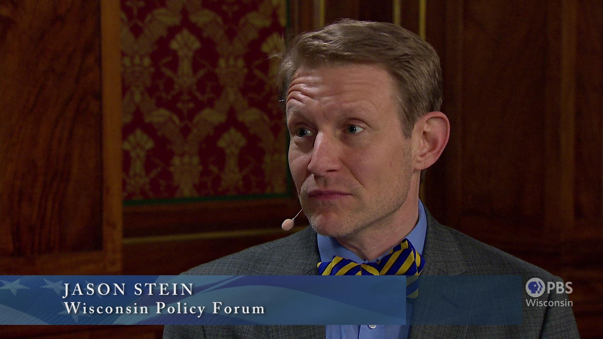 A still image from a video shows Jason Stein speaking into a headset microphone while seated in front of wood paneling, with a graphic at bottom reading 'Jason Stein' and 'Wisconsin Policy Forum.'