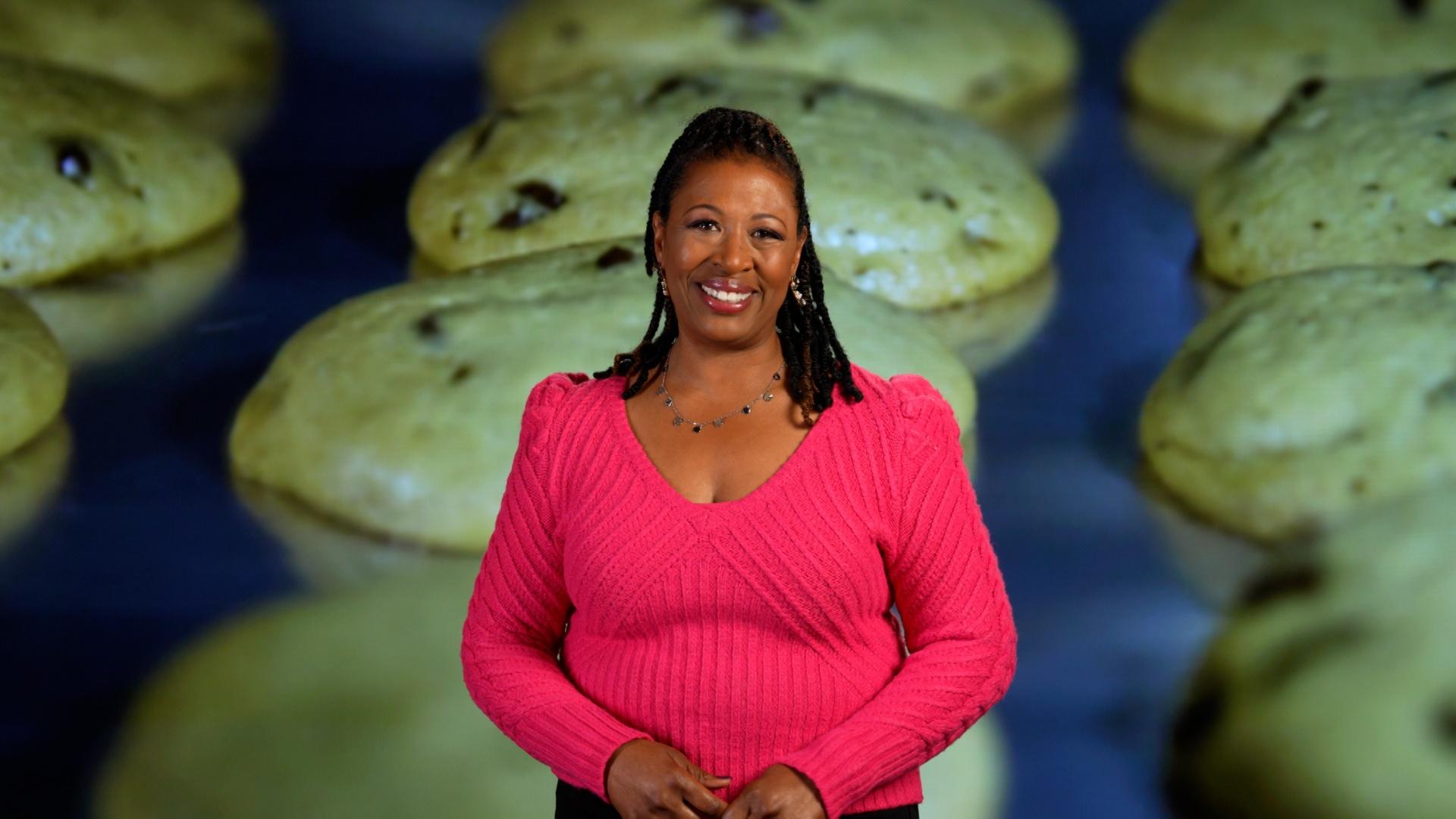 Host of NC Weekend Deborah Holt Noel in front of an image of fresh baked chocolate chip cookies on a baking sheet.