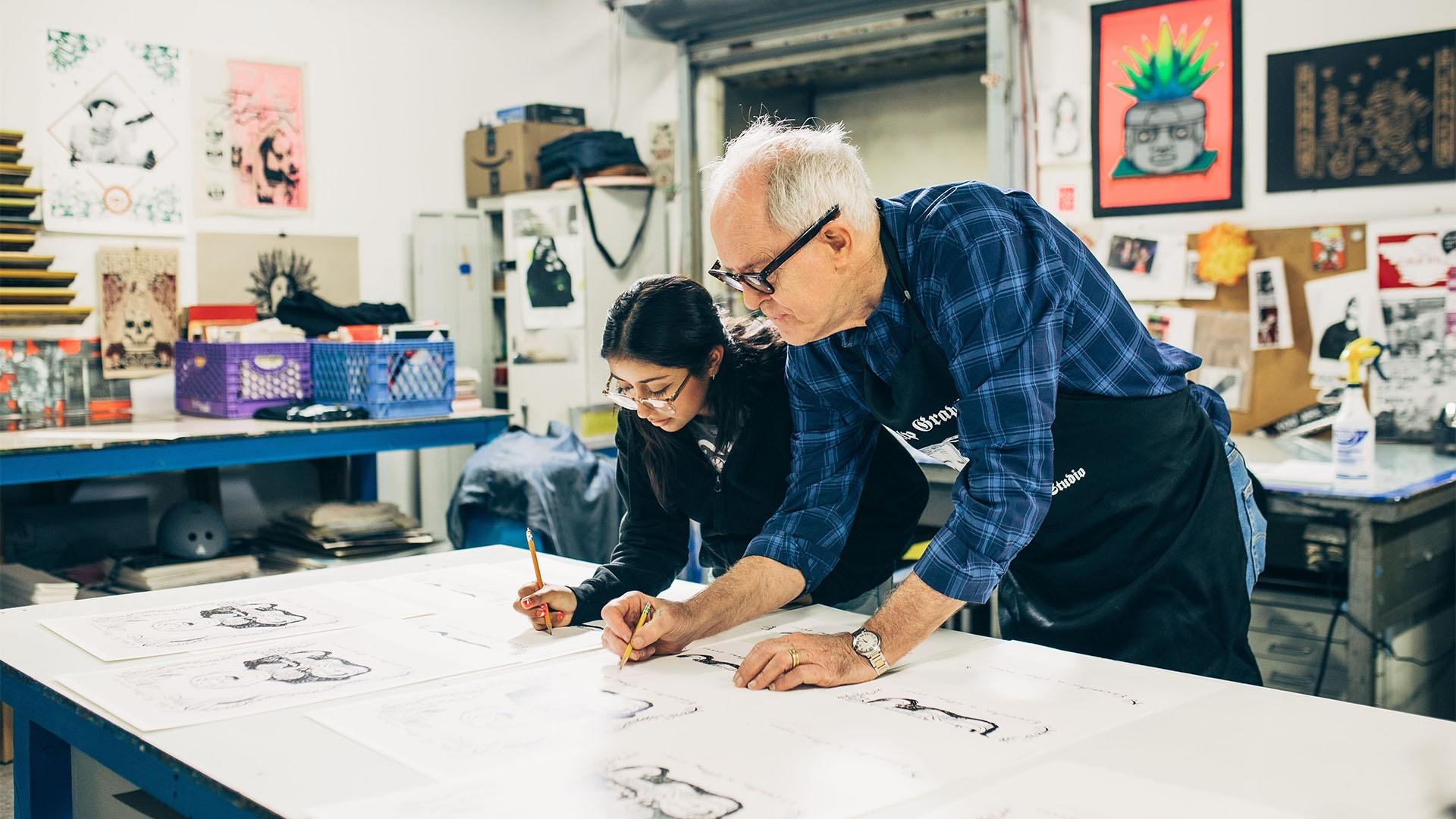 John Lithgow in an illustration studio with a student, each drawing on their own paper surrounded by art