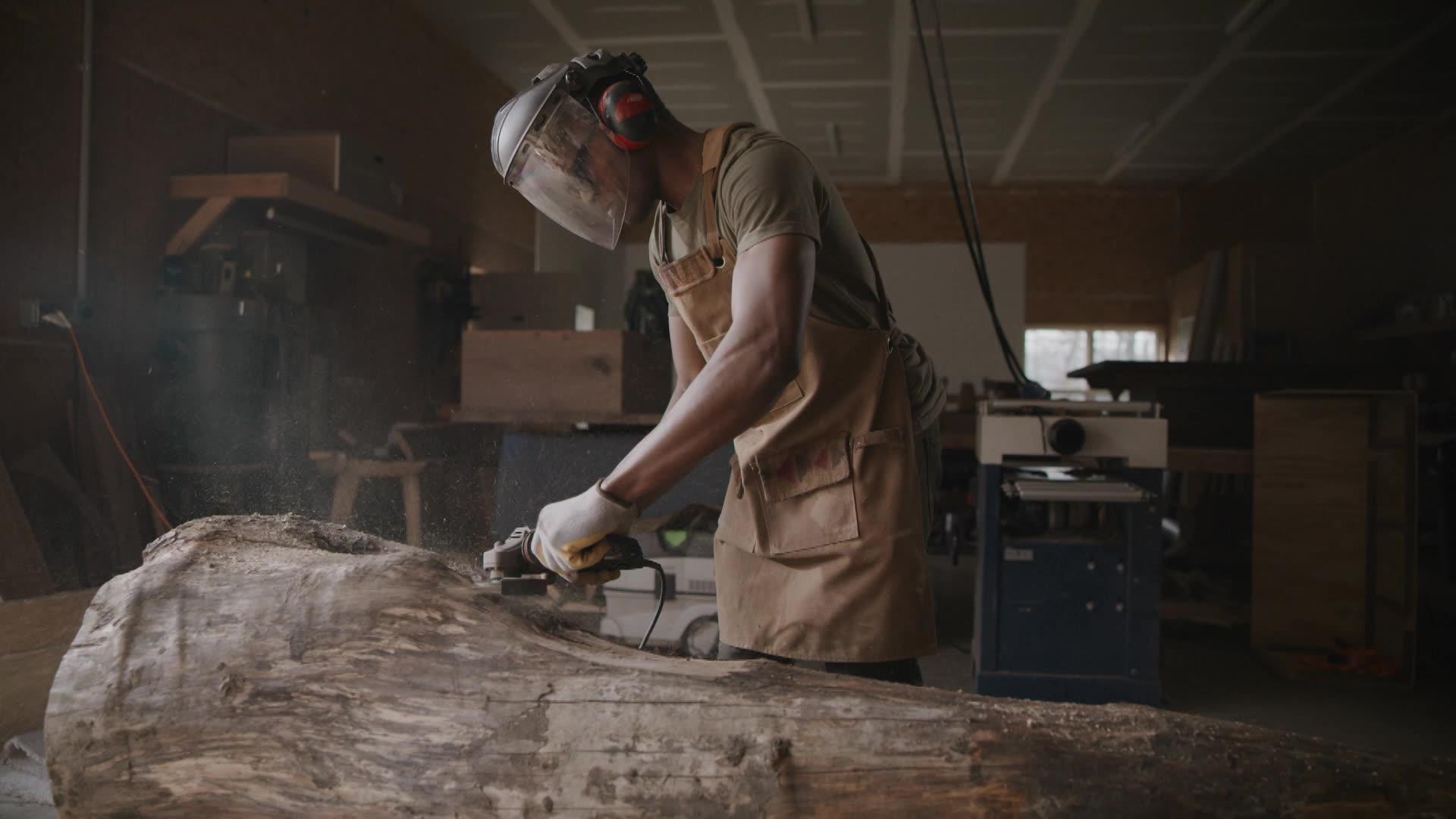 A Black man wearing a protective face shield while carving into a large tree trunk.