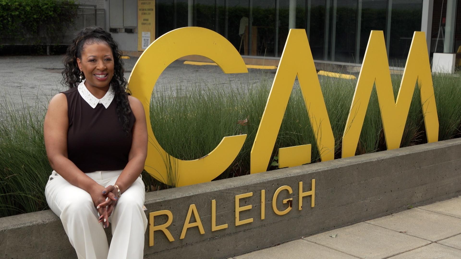 Host of NC Weekend Deborah Holt Noel sitting on a concrete fence out side of the Contemporary Art Museum of Raleigh.