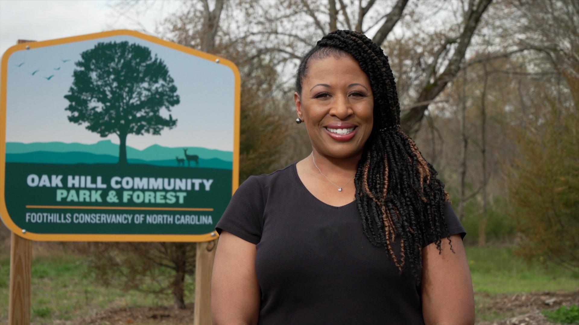 Deborah Holt Noel with the Oak Hill Community Park & Forest sign behind her.