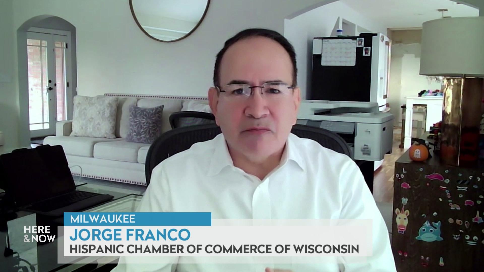 A still image from a video shows Jorge Franco seated in front of a couch with pillows, wall decor and a table with lamp and items with a graphic at bottom reading 'Milwaukee,' 'Jorge Franco' and 'Hispanic Chamber of Commerce of Wisconsin.'