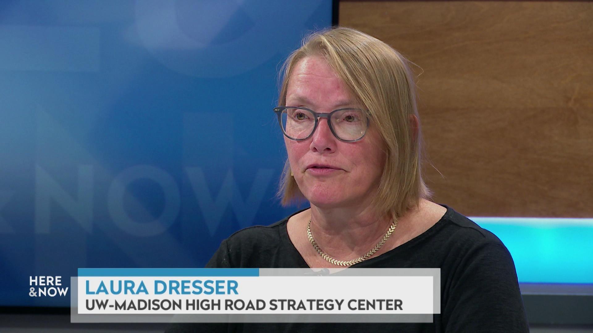A still image shows Laura Dresser seated at the 'Here & Now' set featuring wood paneling, with a graphic at bottom reading 'Laura Dresser' and 'UW-Madison High Road Strategy Center'