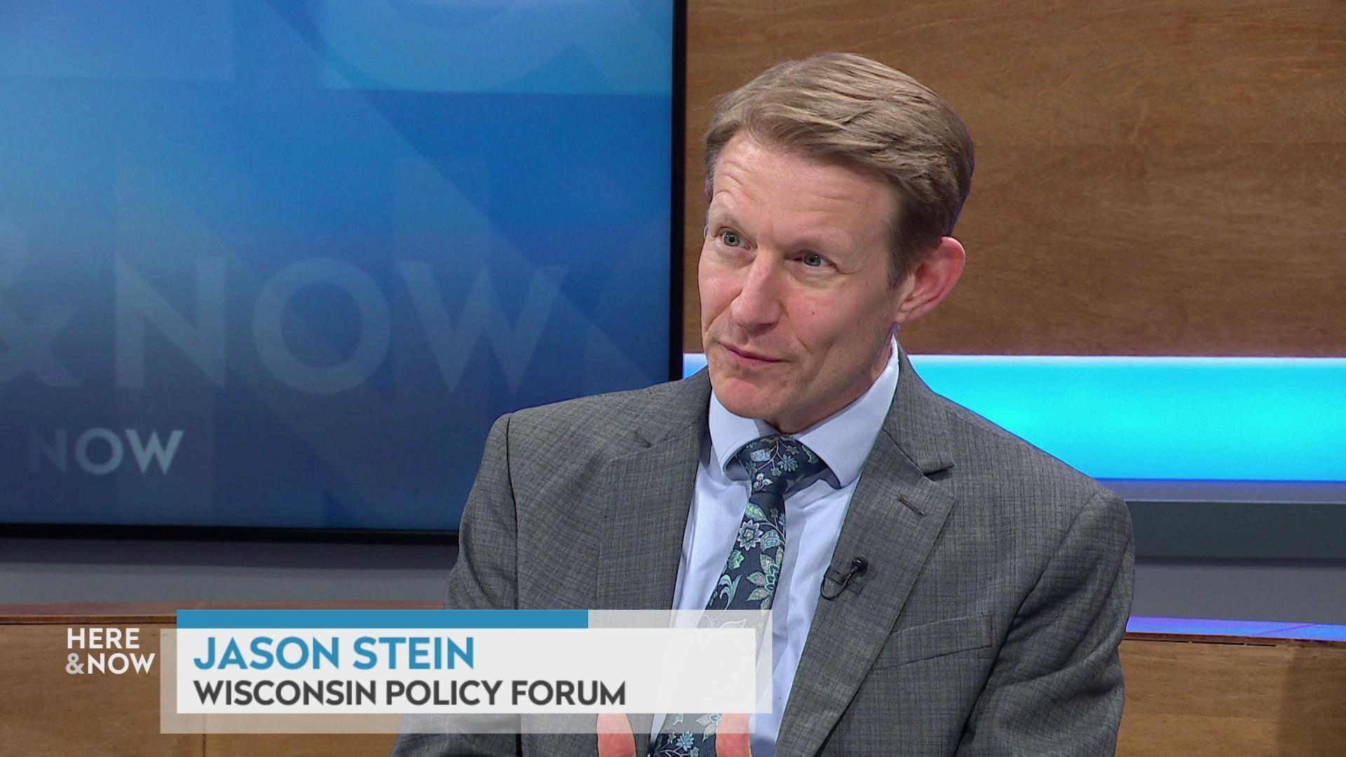 A still image shows Jason Stein seated at the 'Here & Now' set featuring wood paneling, with a graphic at bottom reading 'Jason Stein' and 'Wisconsin Policy Forum.'