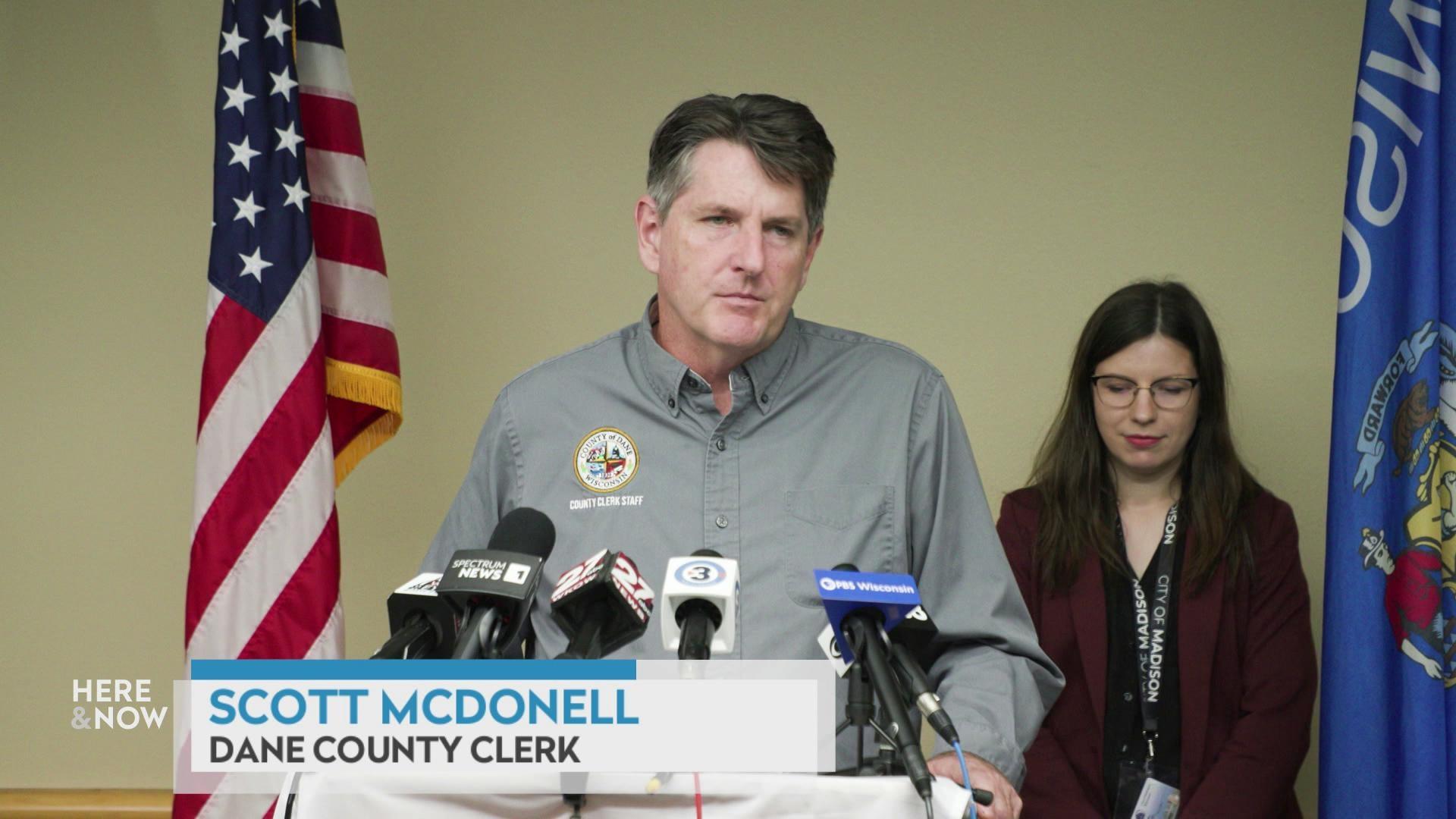 A still image shows Scott McDonell standing in front of a podium with various news mics, with a graphic at the bottom that reads 'Scott McDonell' and 'Dane County Clerk.'