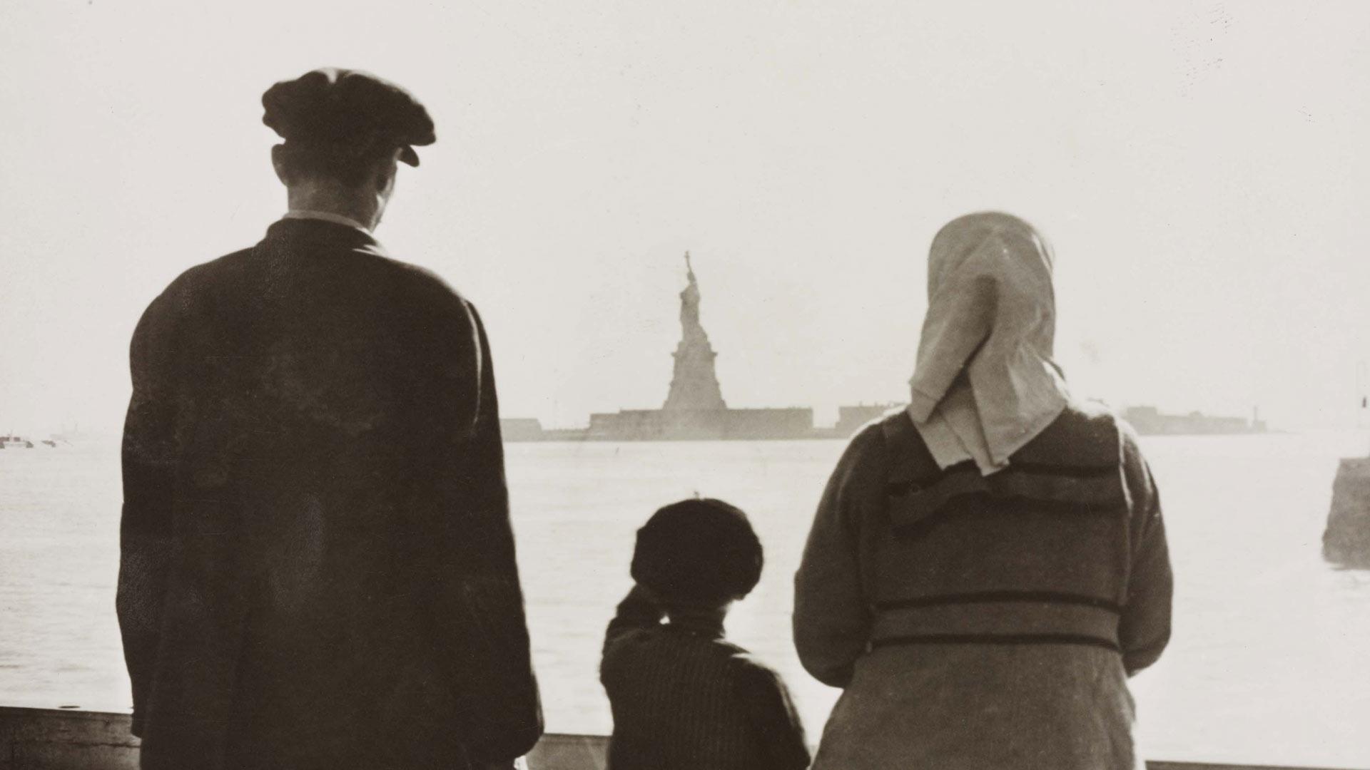 Jewish family stands, facing away from the camera, looking at the Statue of Liberty in the background