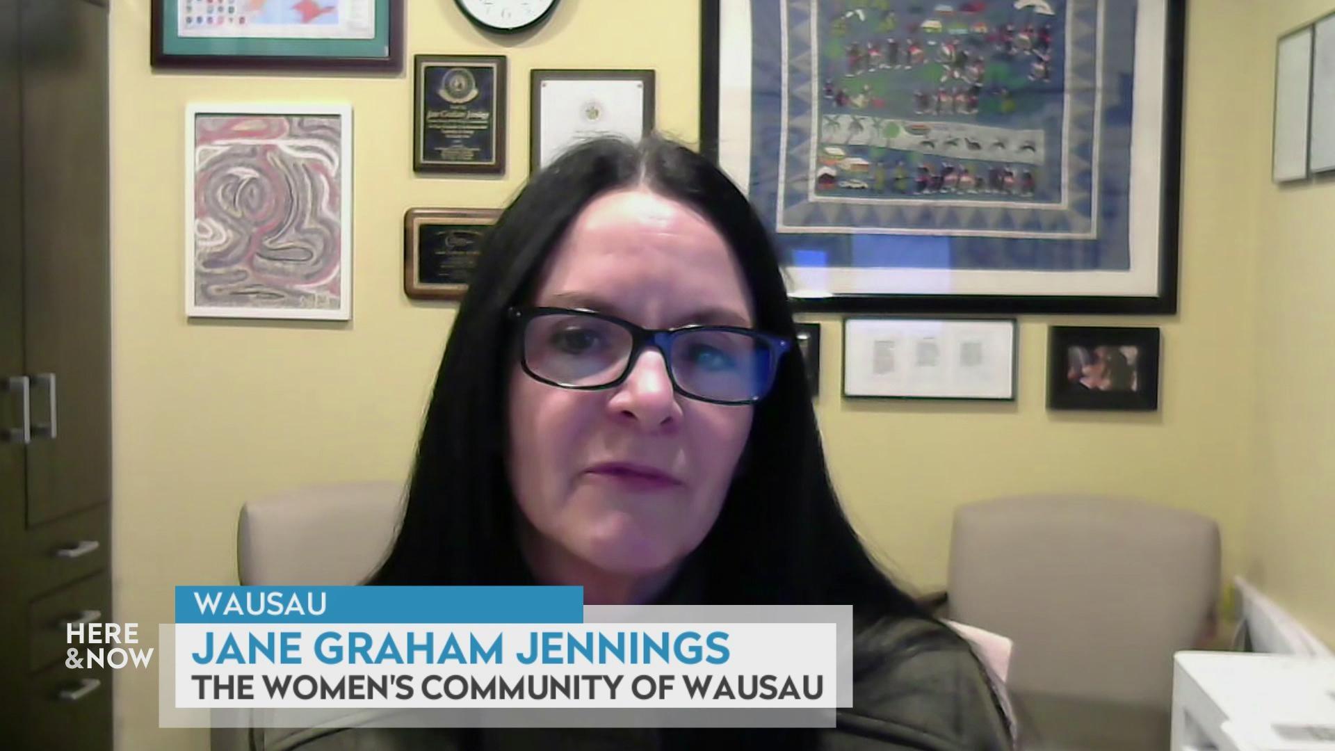 A still image from a video shows Jane Graham Jennings seated in front of a wall with various framed art and chairs in the background with a graphic at bottom reading 'Wausau,' 'Jane Graham Jennings' and 'The Women's Community of Wausau.'