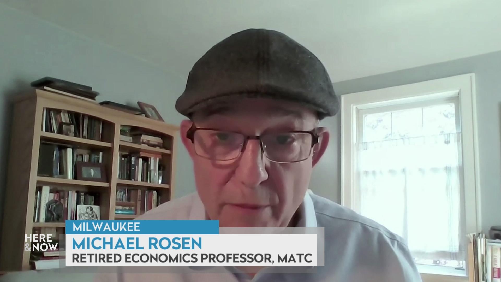 A still image from a video shows Michael Rosen seated in front of a wooden bookshelf lined with books and artwork with a graphic at bottom reading 'Milwaukee,' 'Michael Rosen' and 'Retired Economics Professor, MATC.'