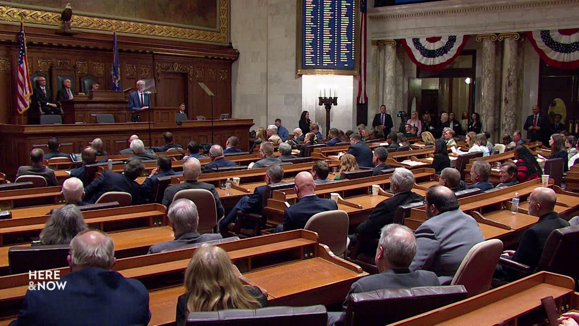 Tony Evers addresses a room full of seated people at podiums during the State of the State.