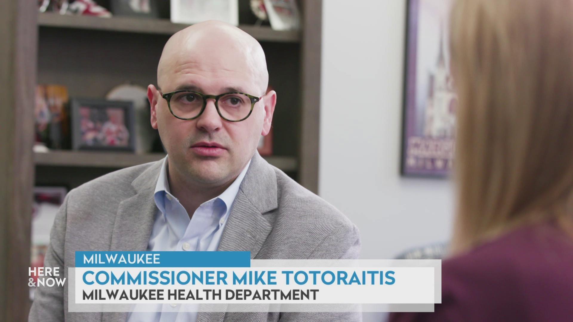 A still image shows Mike Totoraitis seated inside with a wooden bookshelf with framed pictures and item in the background, with a graphic at bottom reading 'Milwaukee,' 'Commissioner Mike Totoraitis' and 'Milwaukee Health Department.'