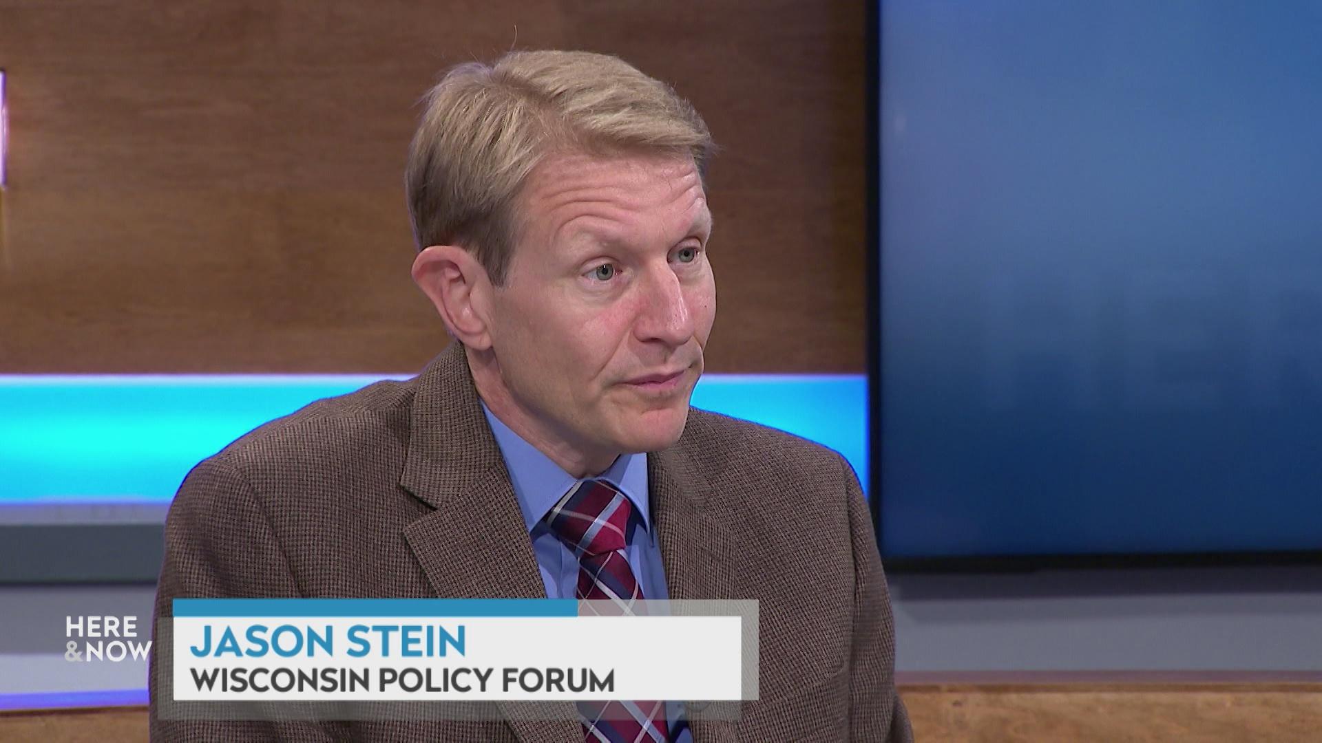 A still image shows Jason Stein seated at the 'Here & Now' set featuring wood paneling, with a graphic at bottom reading 'Jason Stein' and 'Wisconsin Policy Forum.'