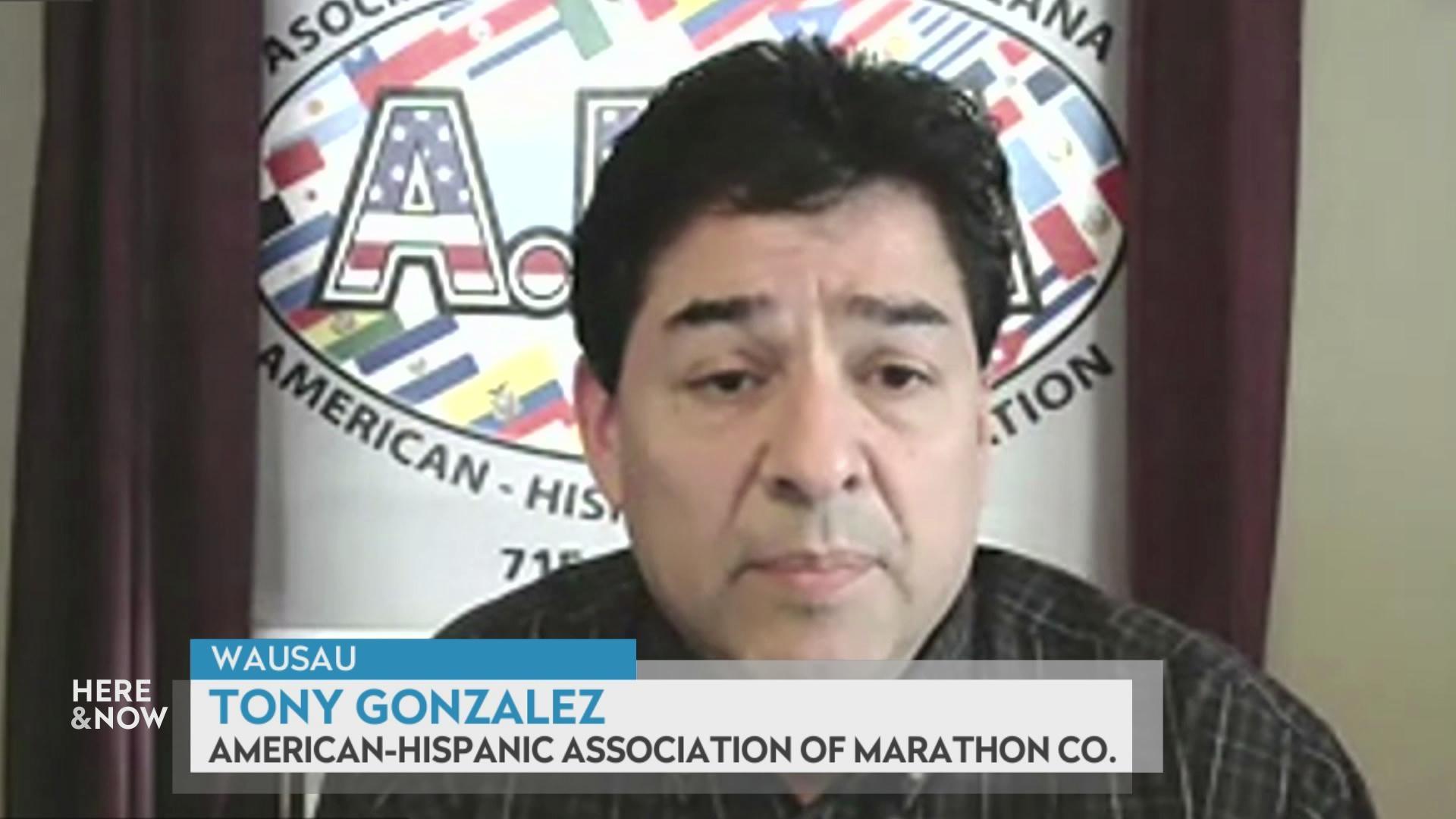 A still image from a video shows Tony Gonzalez seated in front of a wall featuring an American-Hispanic Association logo, with a graphic at bottom reading 'Wausau,' 'Tony Gonzalez' and 'American-Hispanic Association of Marathon Co.'