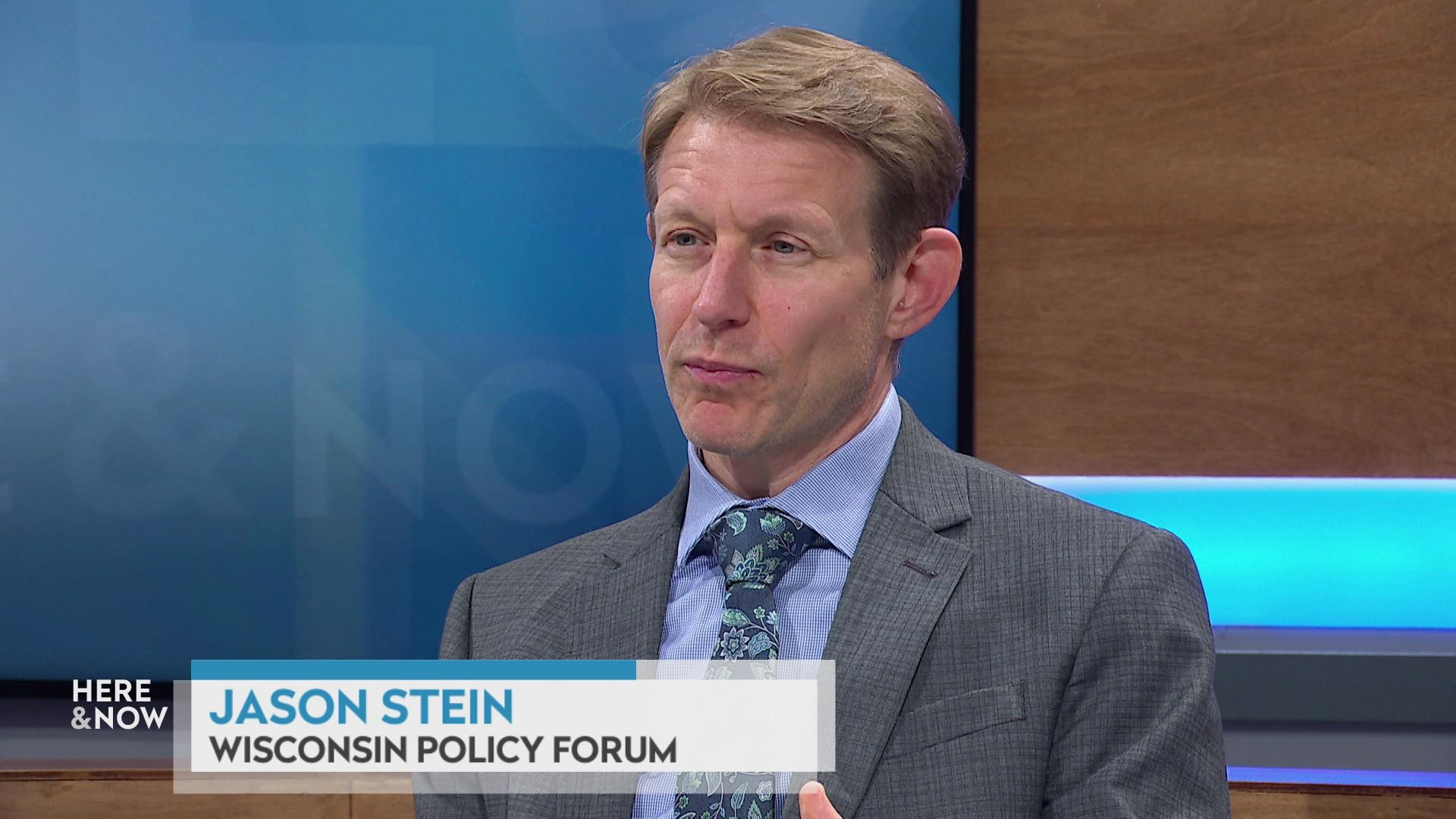 A still image shows Jason Stein seated at the 'Here & Now' set featuring wood paneling, with a graphic at bottom reading 'Jason Stein' and 'Wisconsin Policy Forum.'