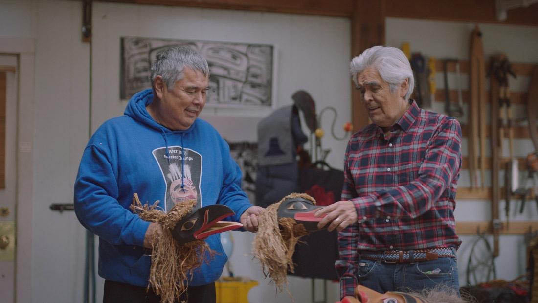 Two men hold Native American ceremonial pieces.