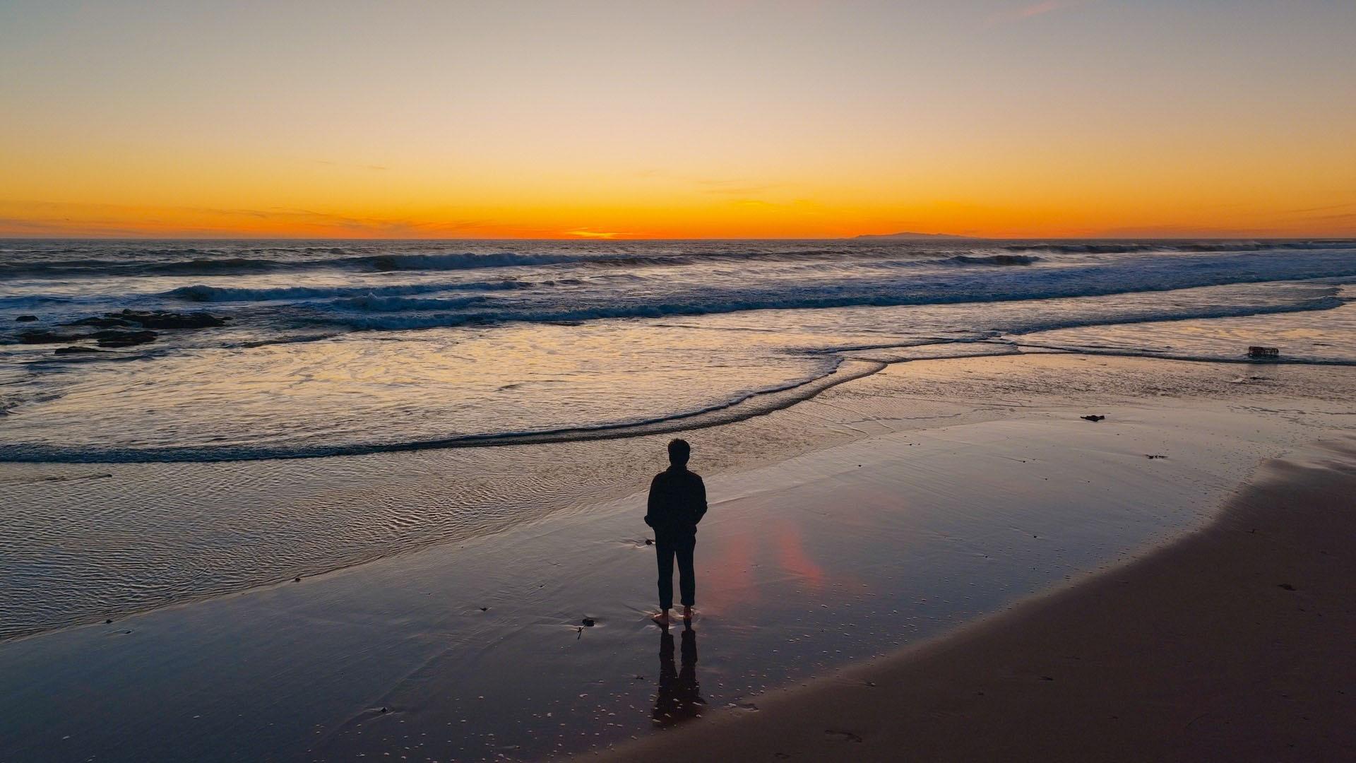 Silhouette of man statnding on shore looking out at sea and sunset