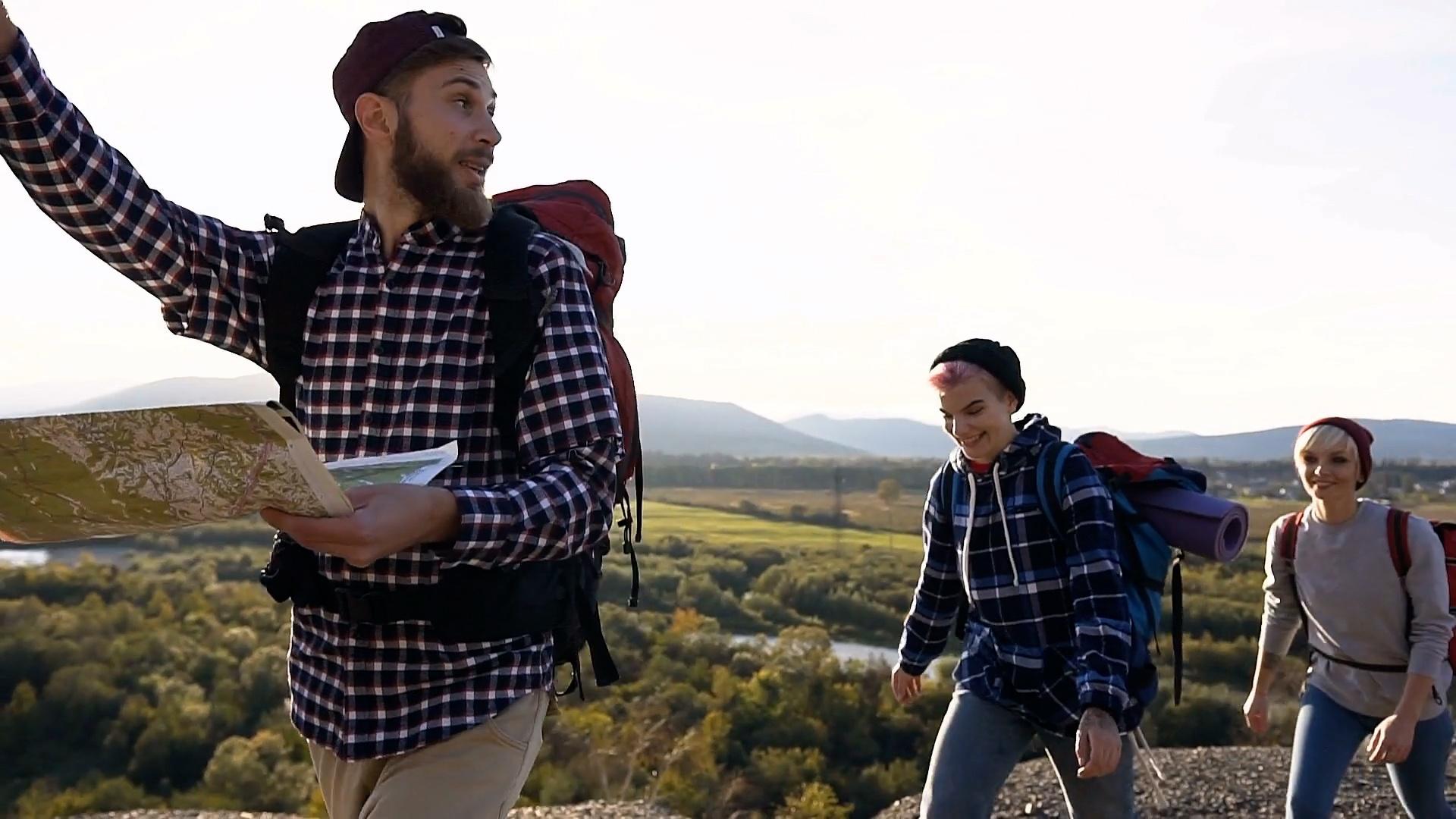 A mountain map maker holding a map and two hikers following.