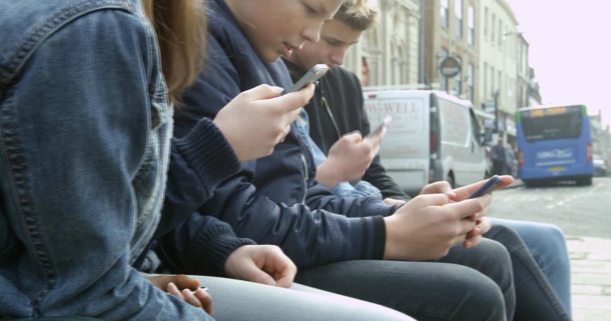 A group of teens sit together and look at their cell phones