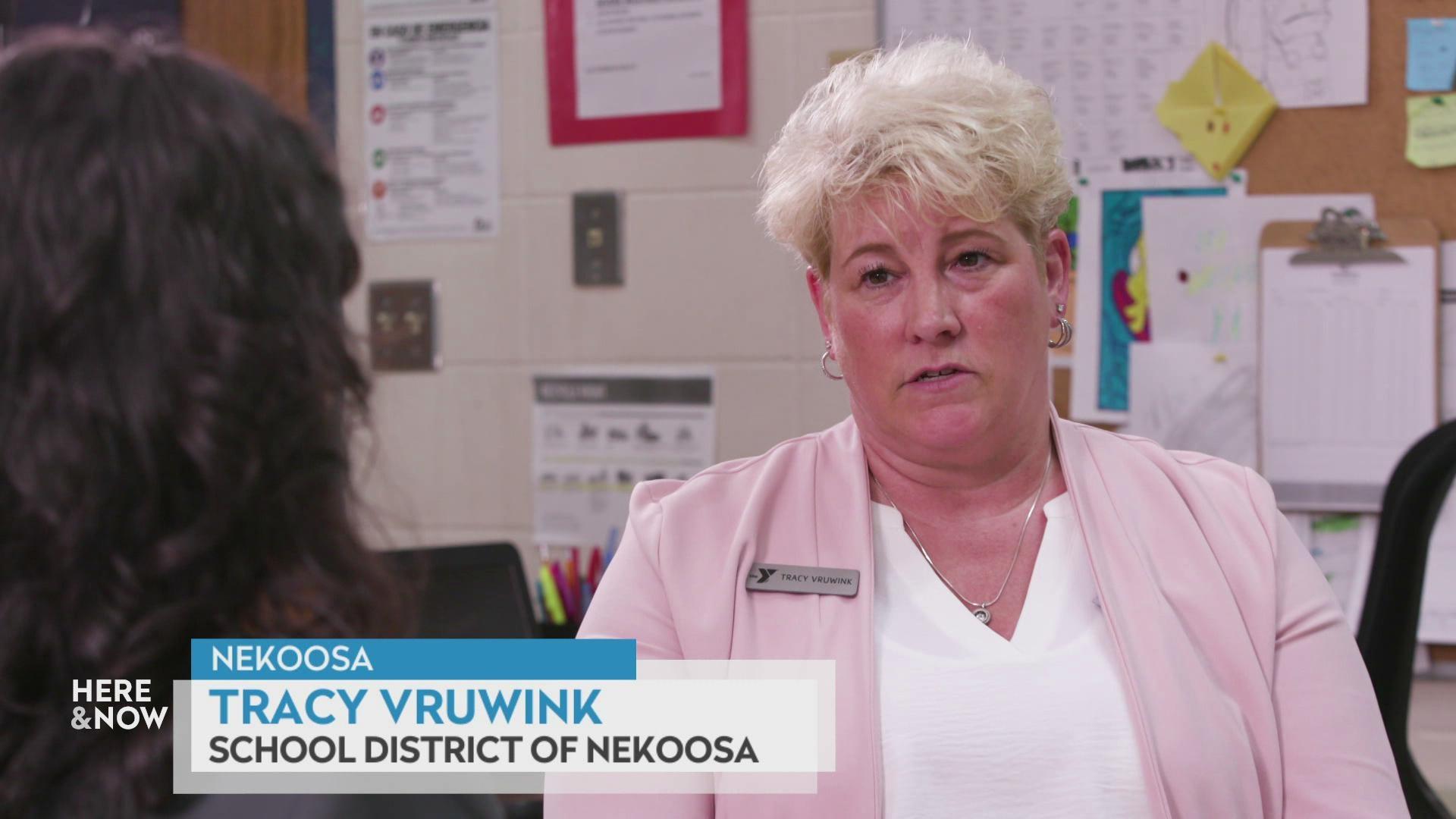 A still image shows Tracy Vruwink sat in front of a white brick walled decorated with lots of school administrative posters, with a graphic in the bottom reading 'Nekoosa,' 'Tracy Vruwink' and 'School district of Nekoosa.'